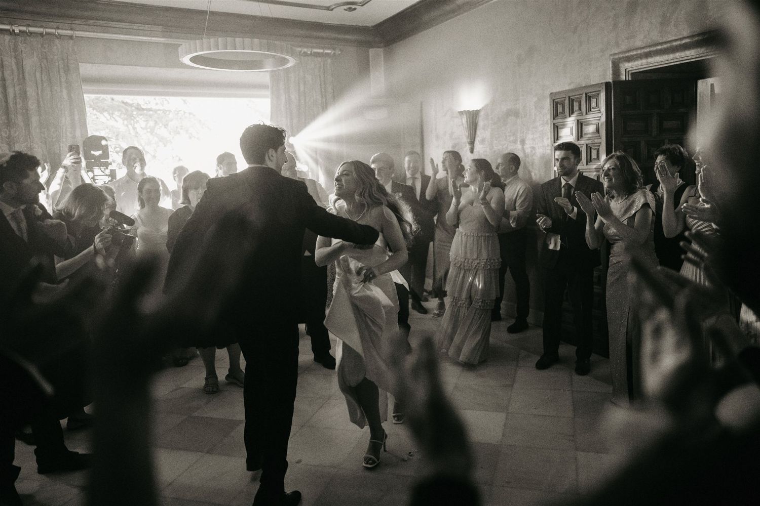 Black and white photo of bride and groom dancing surrounded by cheering wedding guests.