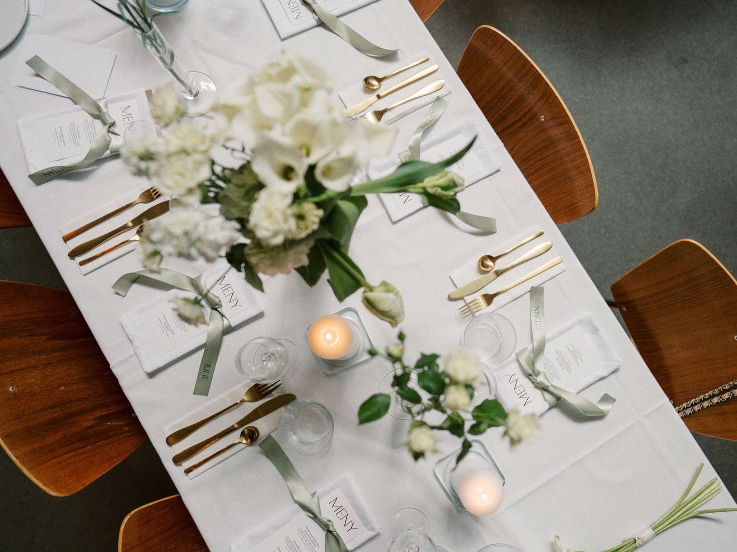 Elegant wedding table setting with white floral centerpieces, gold cutlery, candles, and a white linen runner.