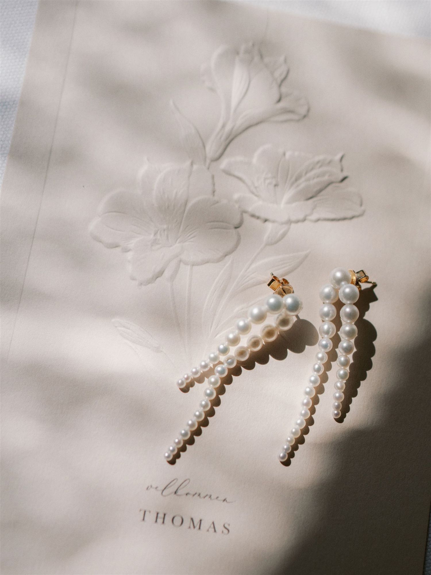 Delicate pearl drop bridal earrings displayed on floral embossed stationery with elegant script.