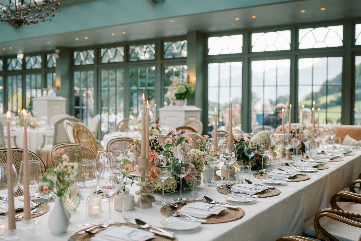 Elegant wedding reception table setting with floral centerpieces, candles, and gold accents in a greenhouse venue.