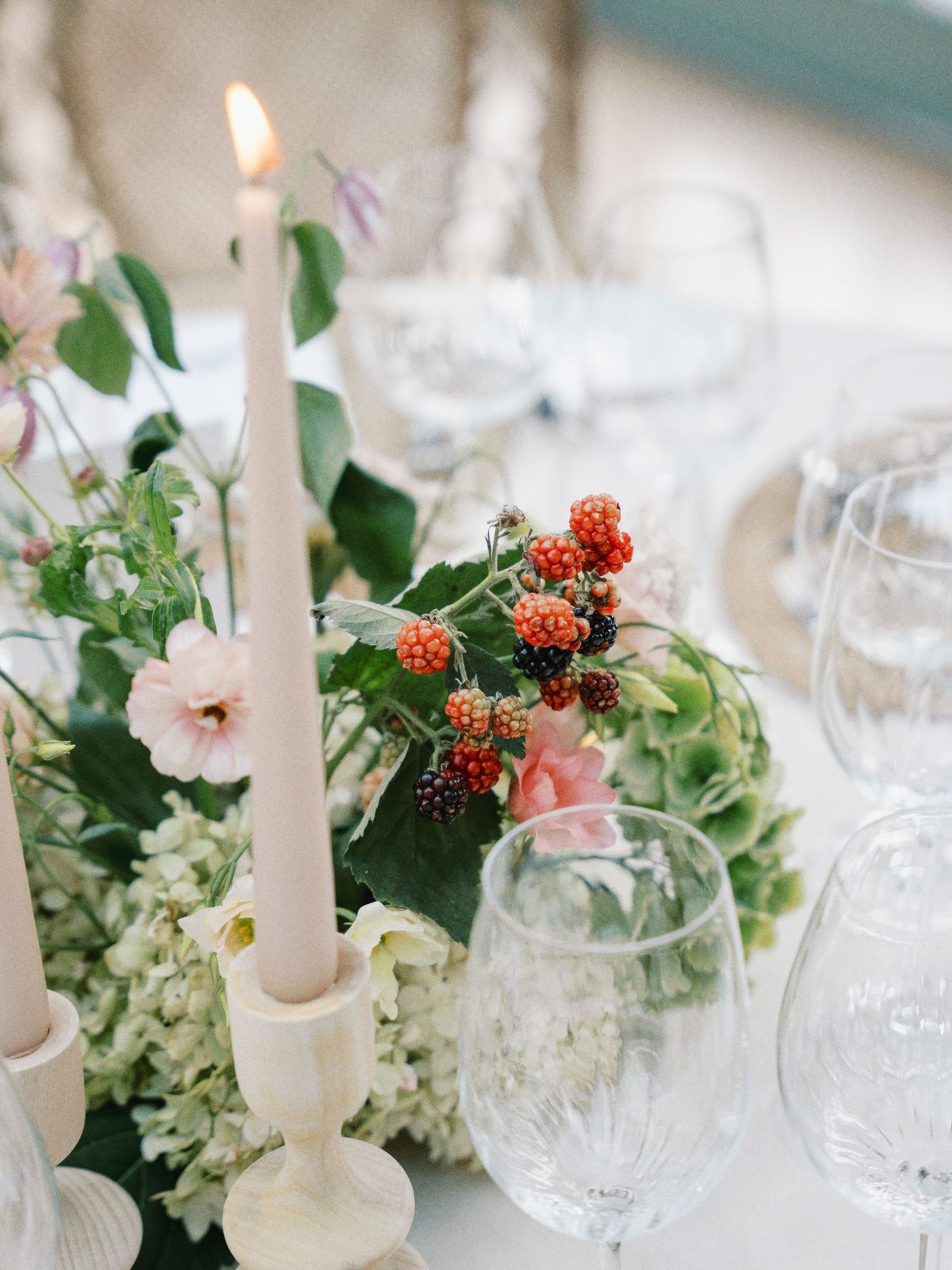 Elegant wedding tablescape with white hydrangeas, red berries, pink blooms, lit taper candles, and crystal glassware.