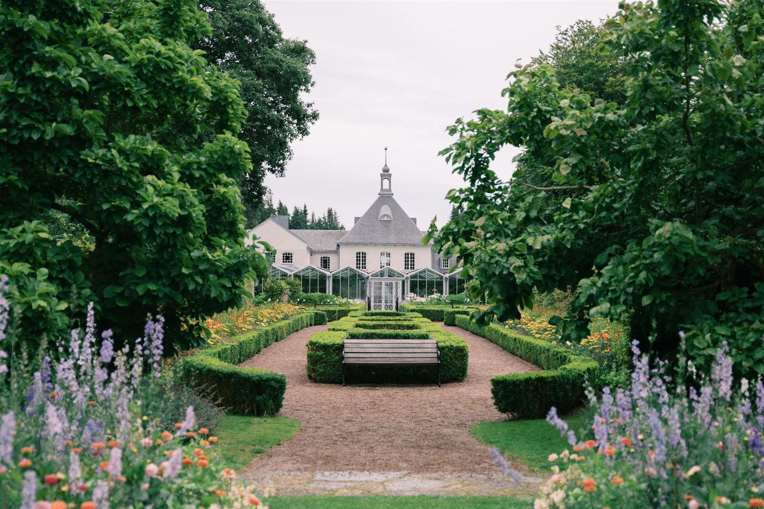 Elegant French chateau with formal boxwood garden, colorful flowers, and gravel pathway.