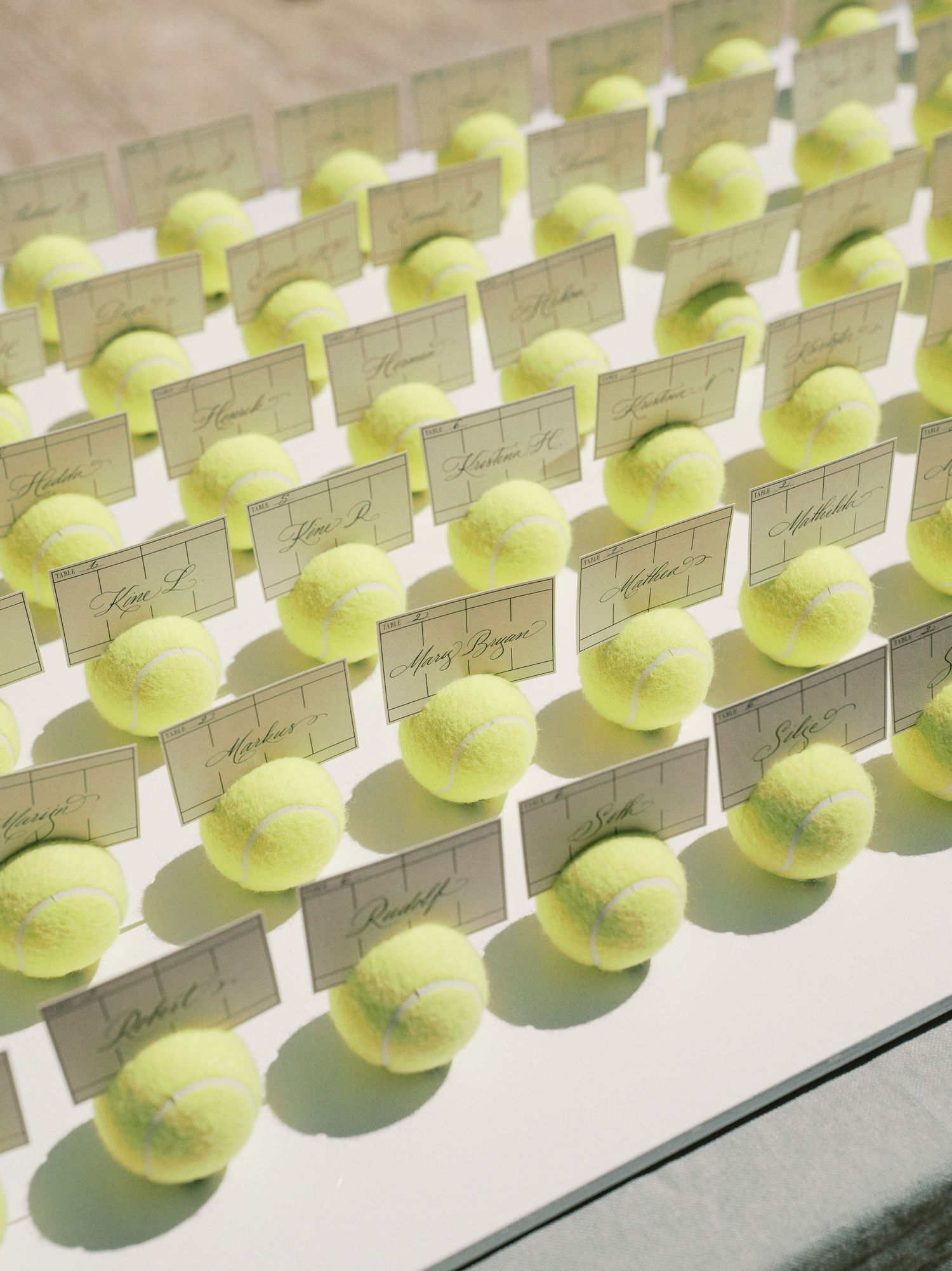 Tennis ball place card holders arranged in rows for a creative wedding reception seating display.