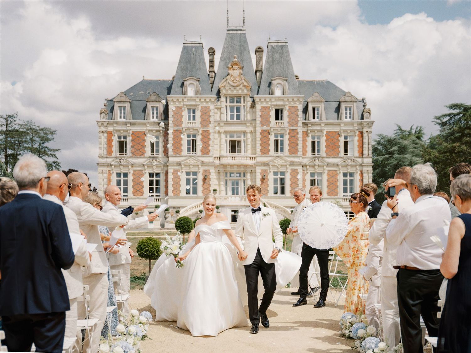Bride and groom exit ceremony at stunning French chateau surrounded by cheering guests.