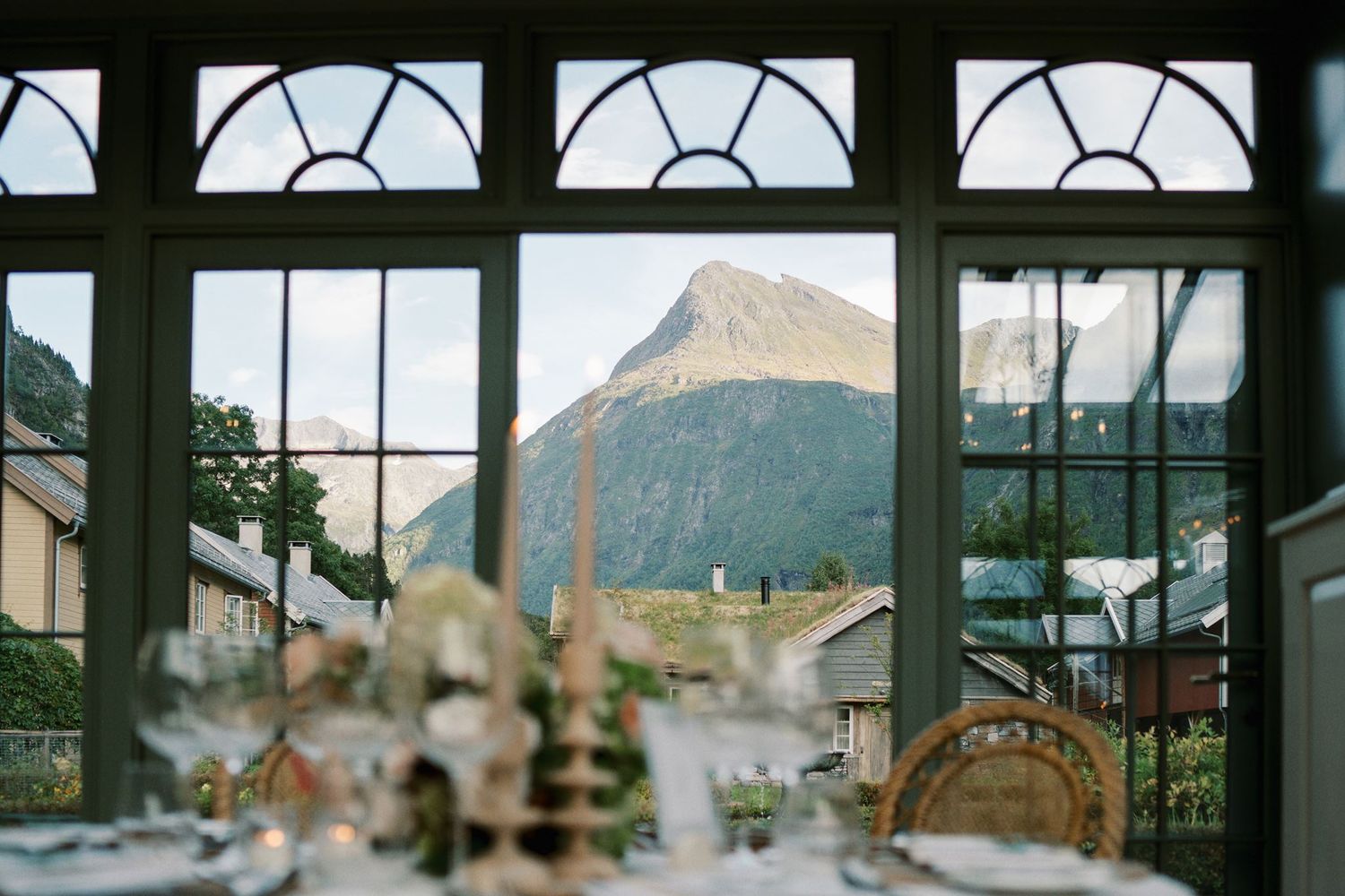 Elegant wedding reception table with mountain view through large windows in a scenic venue.