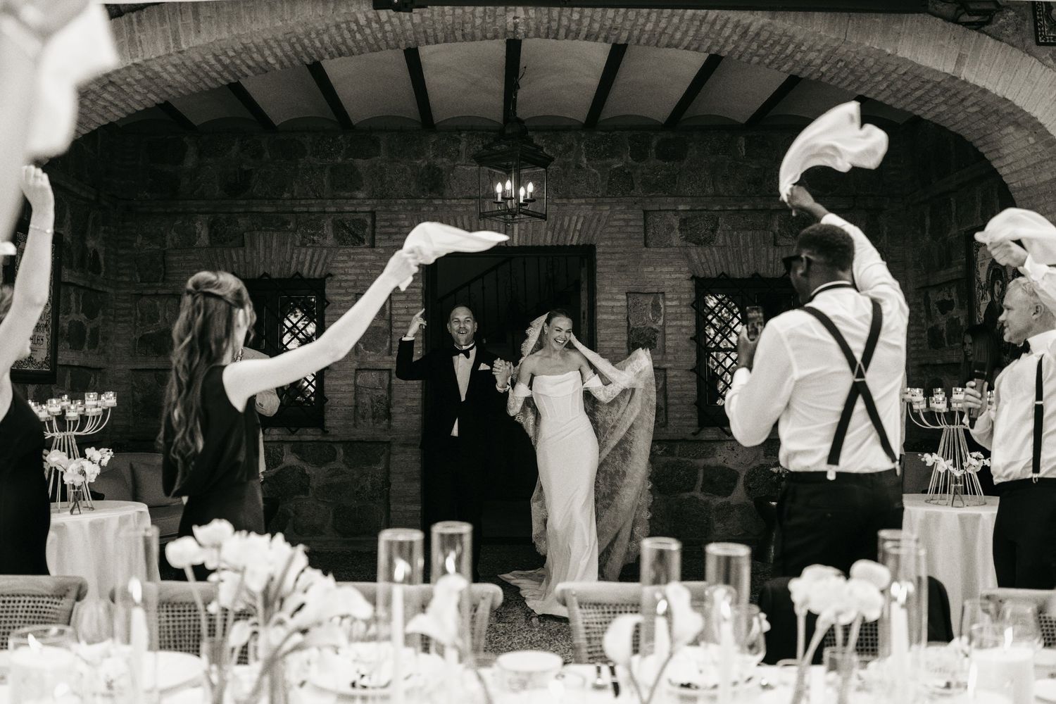 Black and white photo of a wedding couple entering reception hall with guests waving white napkins in celebration.