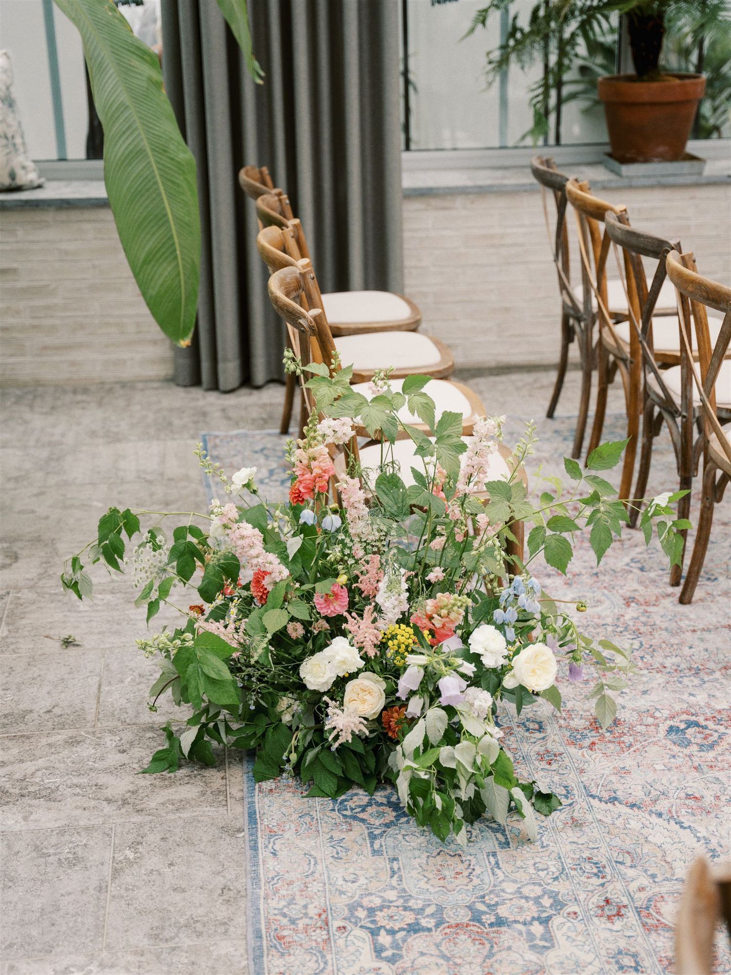 Lush floral arrangement with pink, white, and peach blooms beside wooden ceremony chairs.