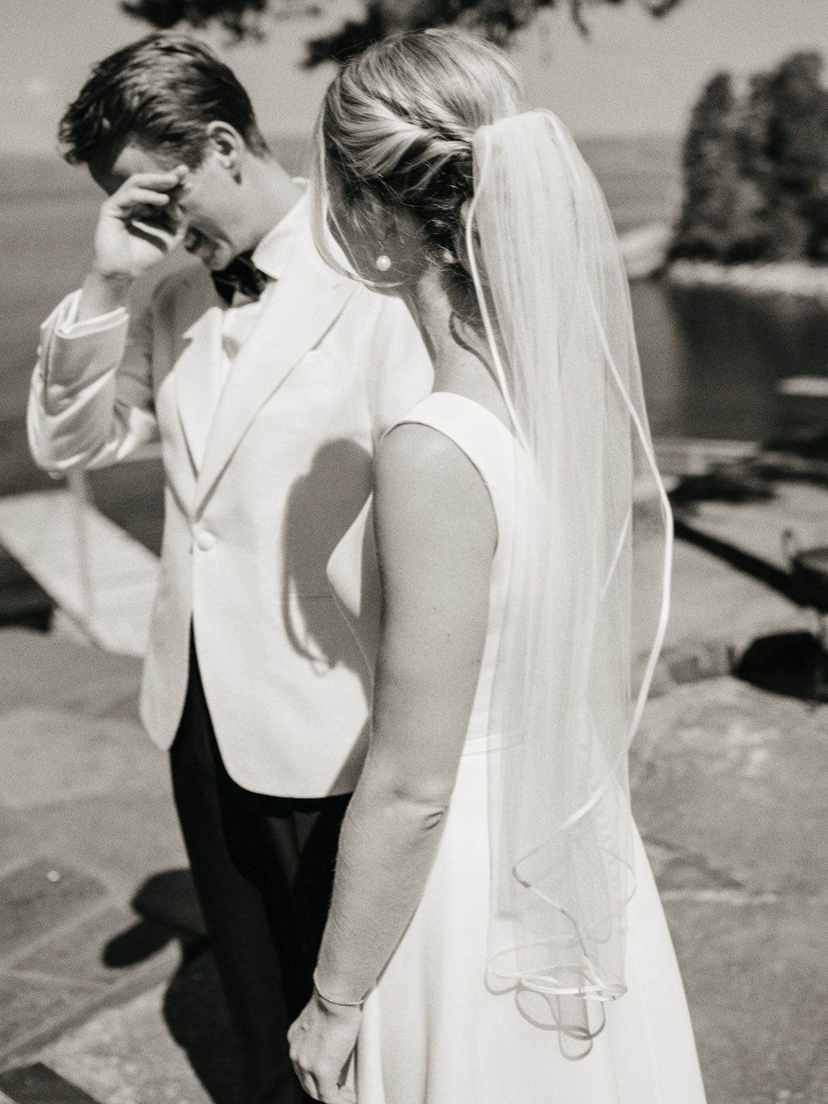 Black and white photo of emotional groom wiping tears seeing bride for first time.