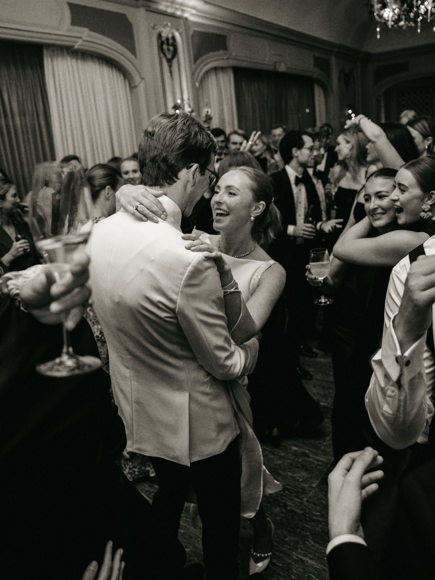 Joyful couple dancing and embracing at a crowded black and white wedding reception party.