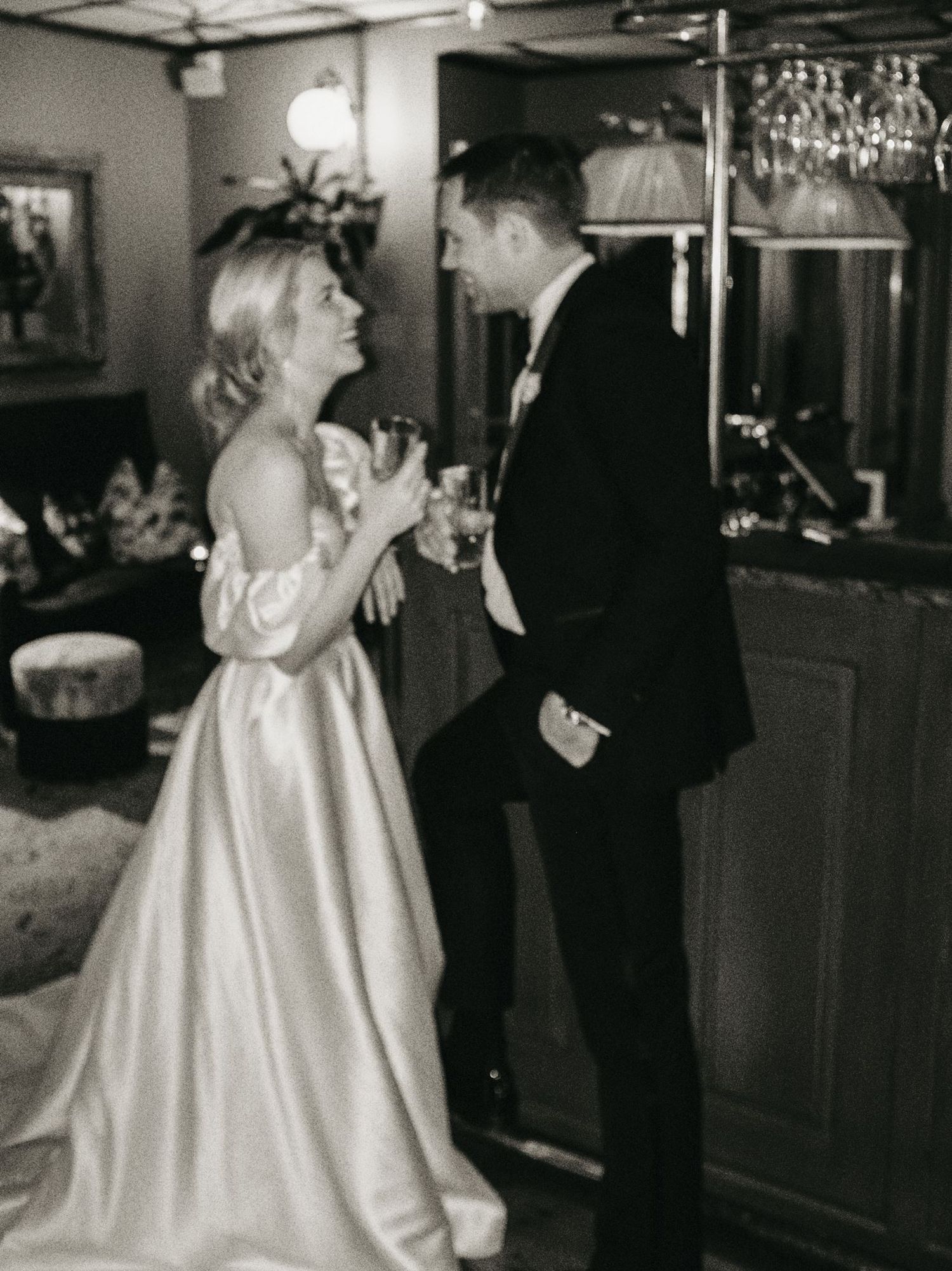 Black and white photo of a bride and groom sharing a toast at their wedding reception in an elegant venue.