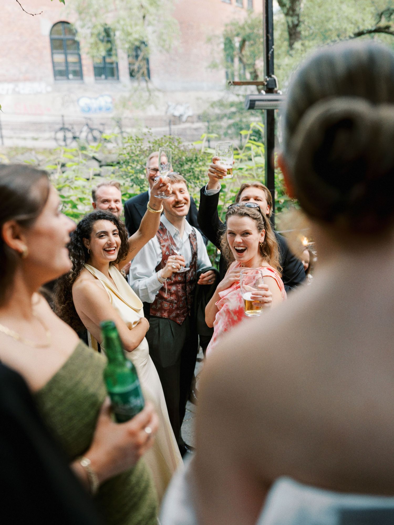 Wedding guests raise glasses in a joyful toast, laughing and celebrating together at an outdoor reception venue.