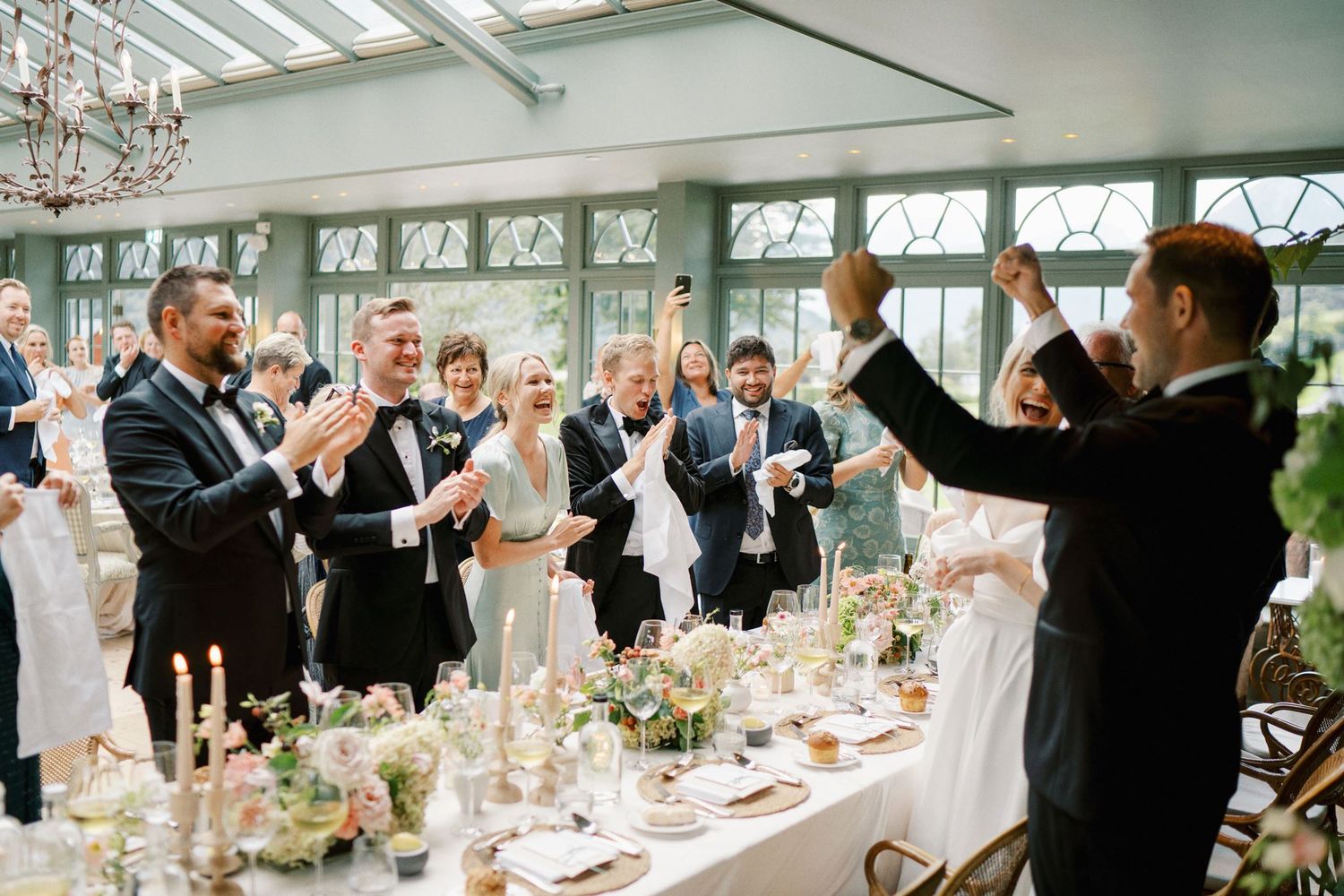 Elegant wedding reception toast in a bright conservatory with guests in formal attire celebrating.