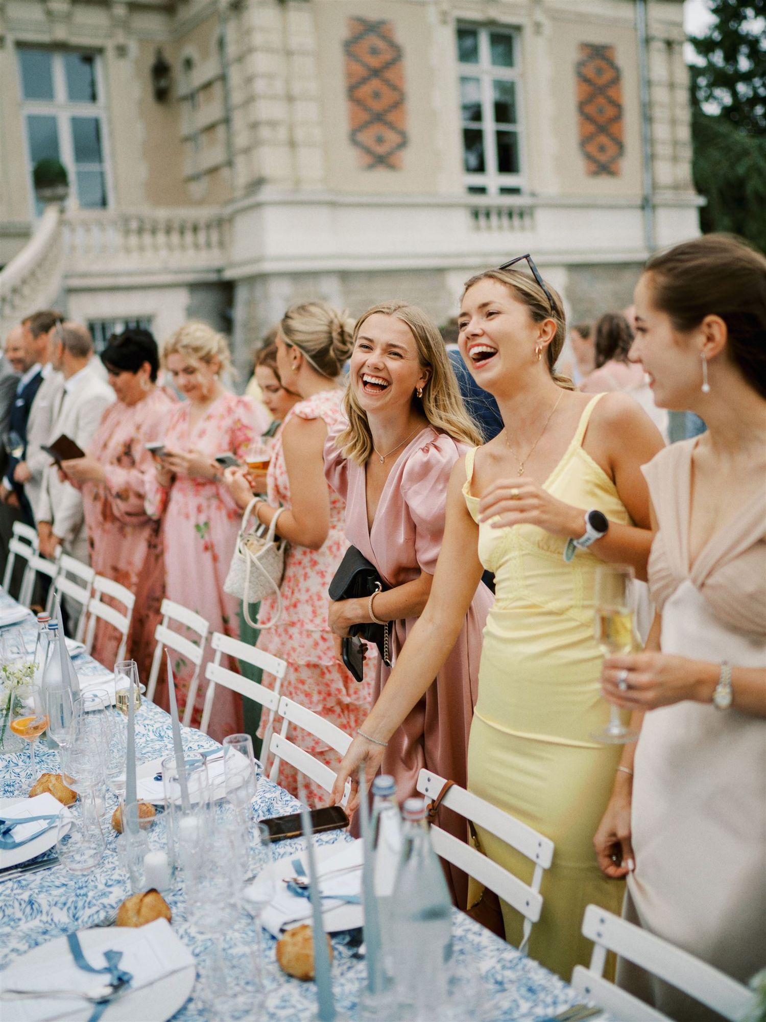 Wedding guests laughing and celebrating at outdoor reception table at chateau venue.