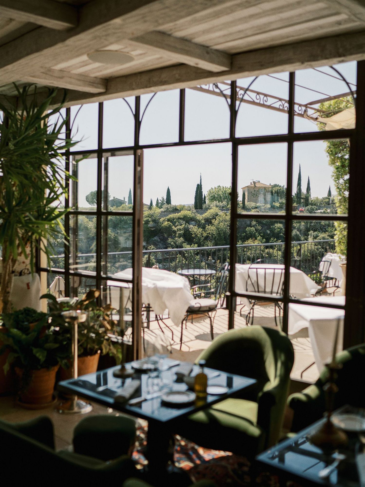 Elegant restaurant interior with large steel windows overlooking lush garden terrace.