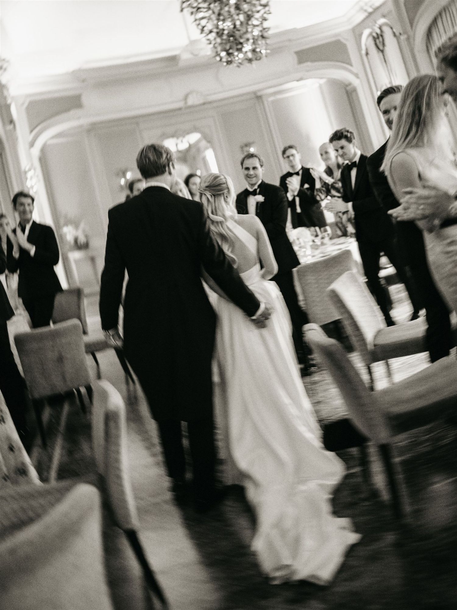 Black and white photo of bride and groom entering wedding reception to cheering guests.