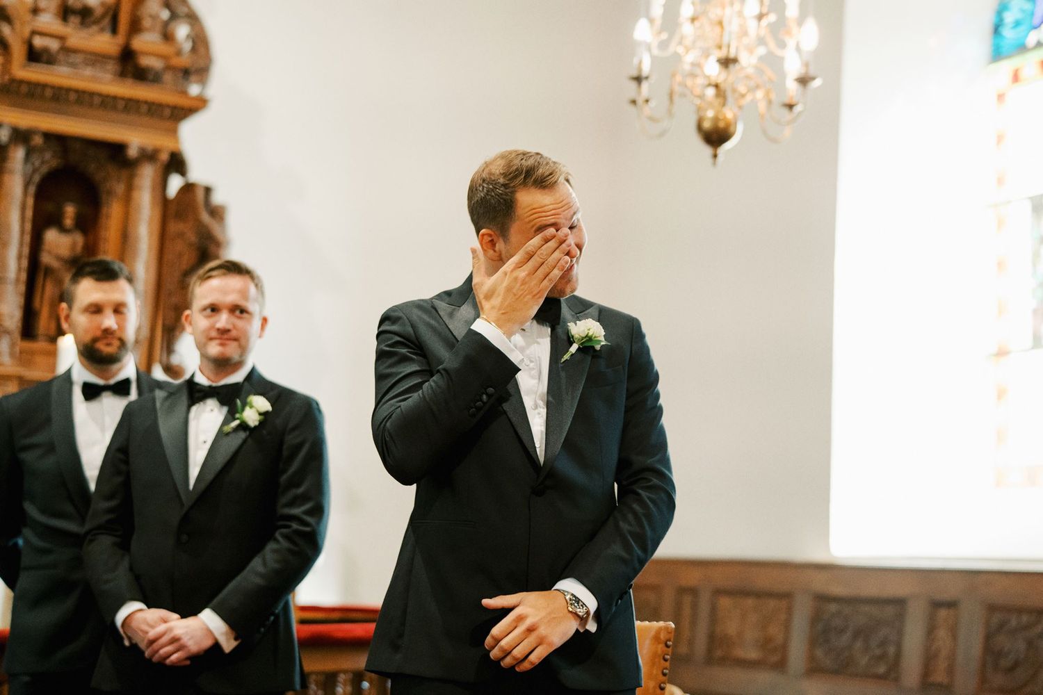 Emotional groom covering his face with his hand at the altar during wedding ceremony in a church.