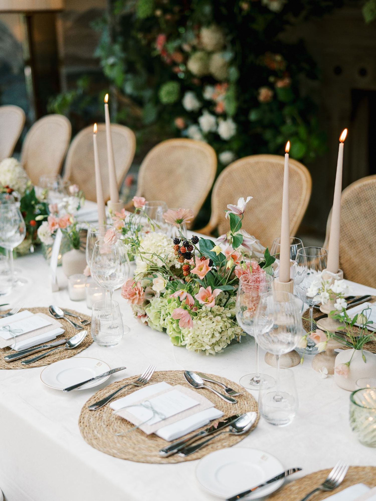 Elegant wedding reception table with floral centerpieces, taper candles, and woven charger plates.