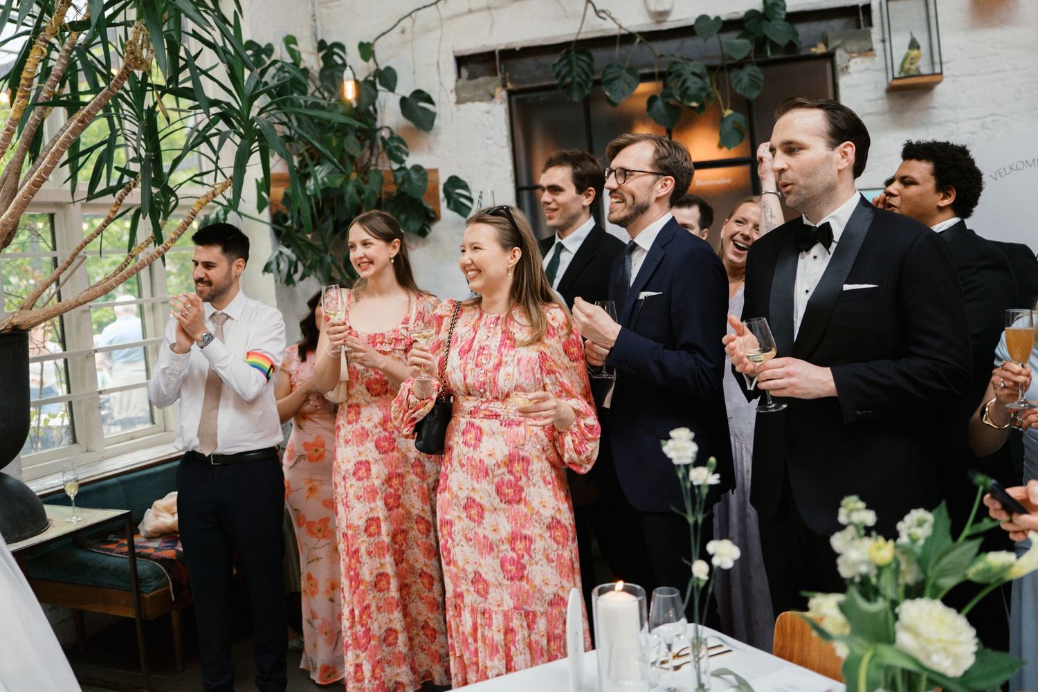 Wedding guests in formal attire clapping and celebrating indoors at a reception venue.