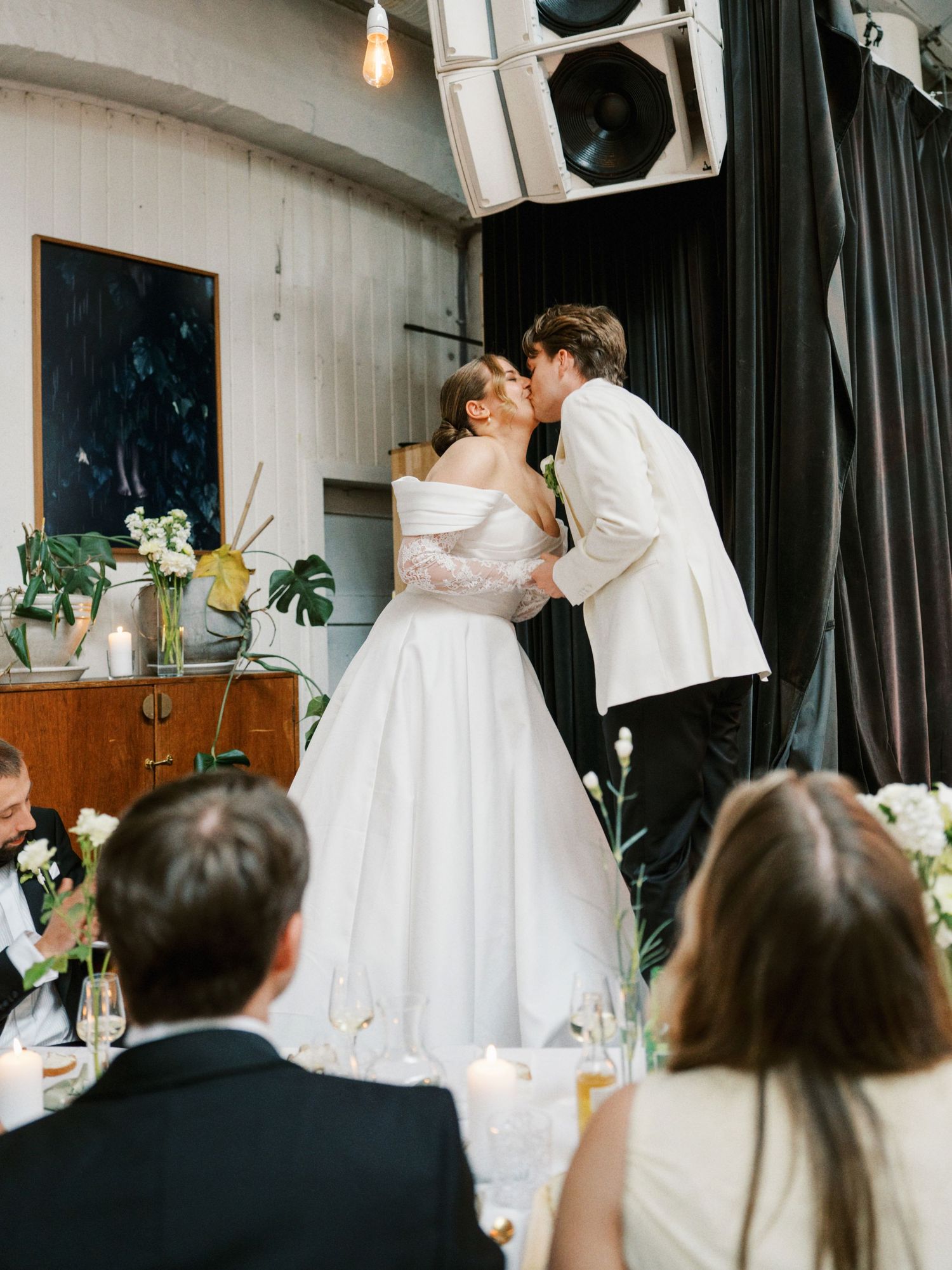 Bride and groom share a kiss at their elegant wedding reception, surrounded by floral arrangements and candlelight.