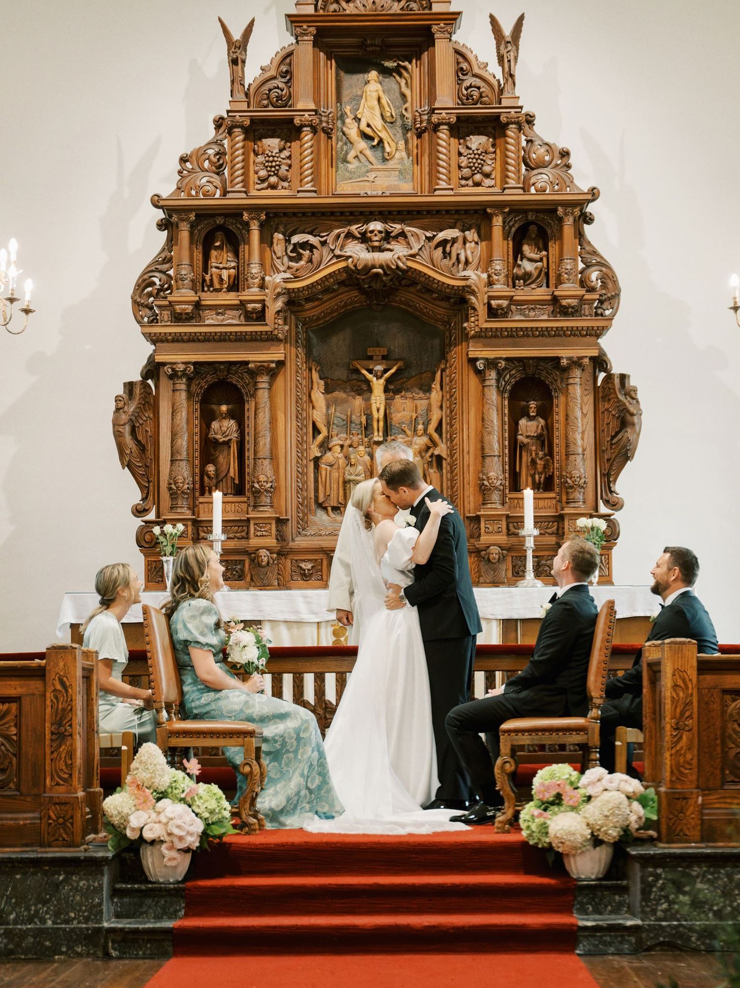 Bride and groom share a kiss at the altar of an ornate wooden church during their wedding ceremony.