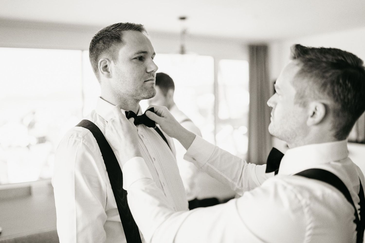 Groom getting bow tie adjusted by groomsman in black and white wedding preparation photo.