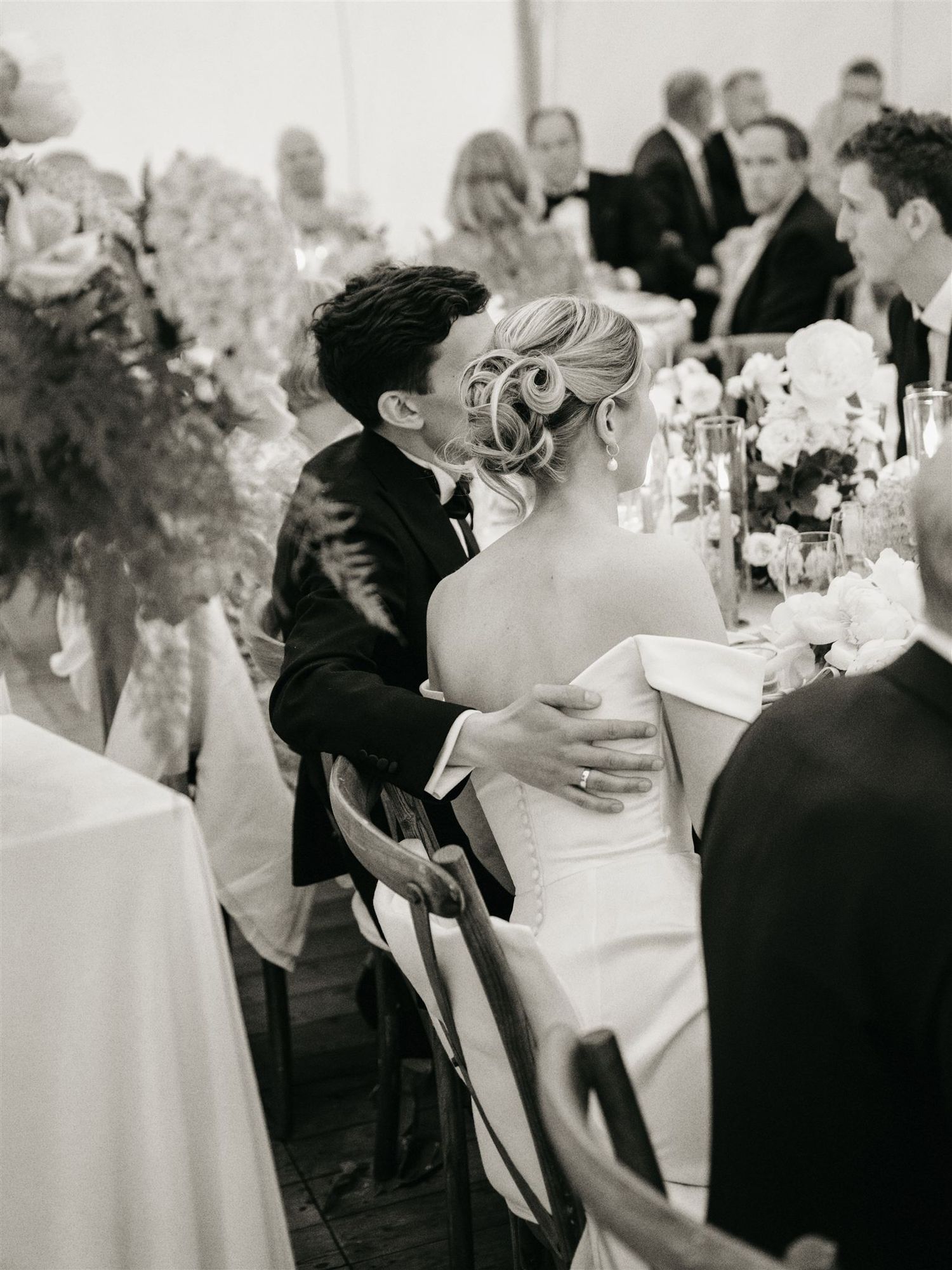 Bride and groom share intimate moment at elegant wedding reception table in black and white photo.