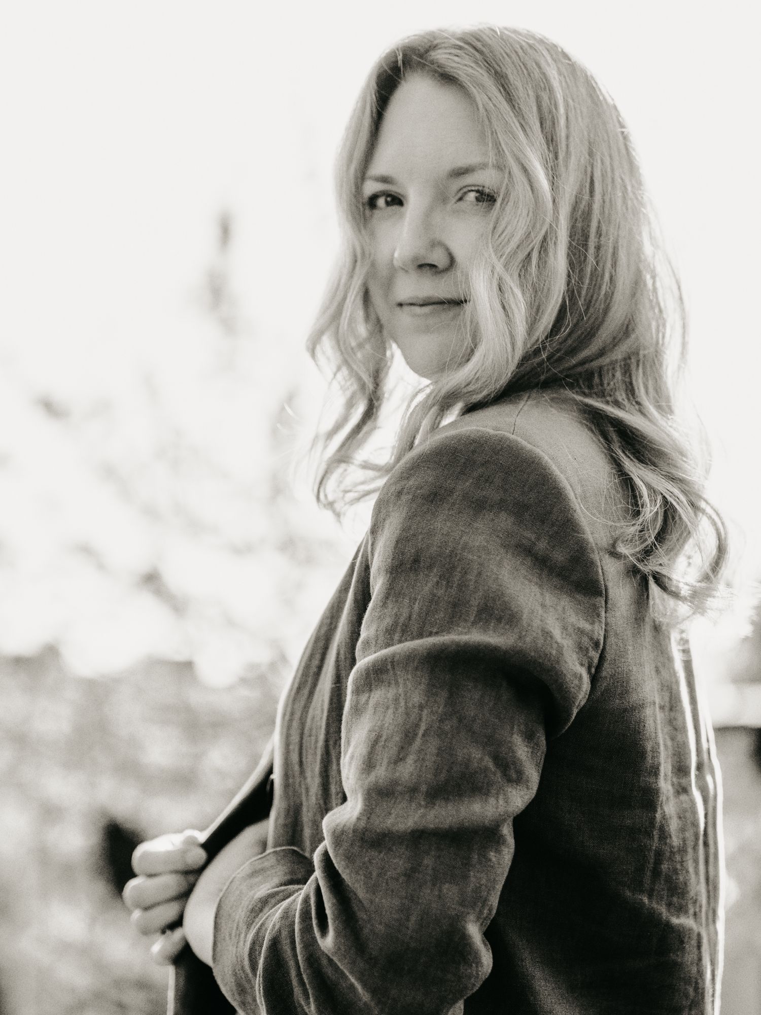 Black and white portrait of blonde woman looking over shoulder outdoors.