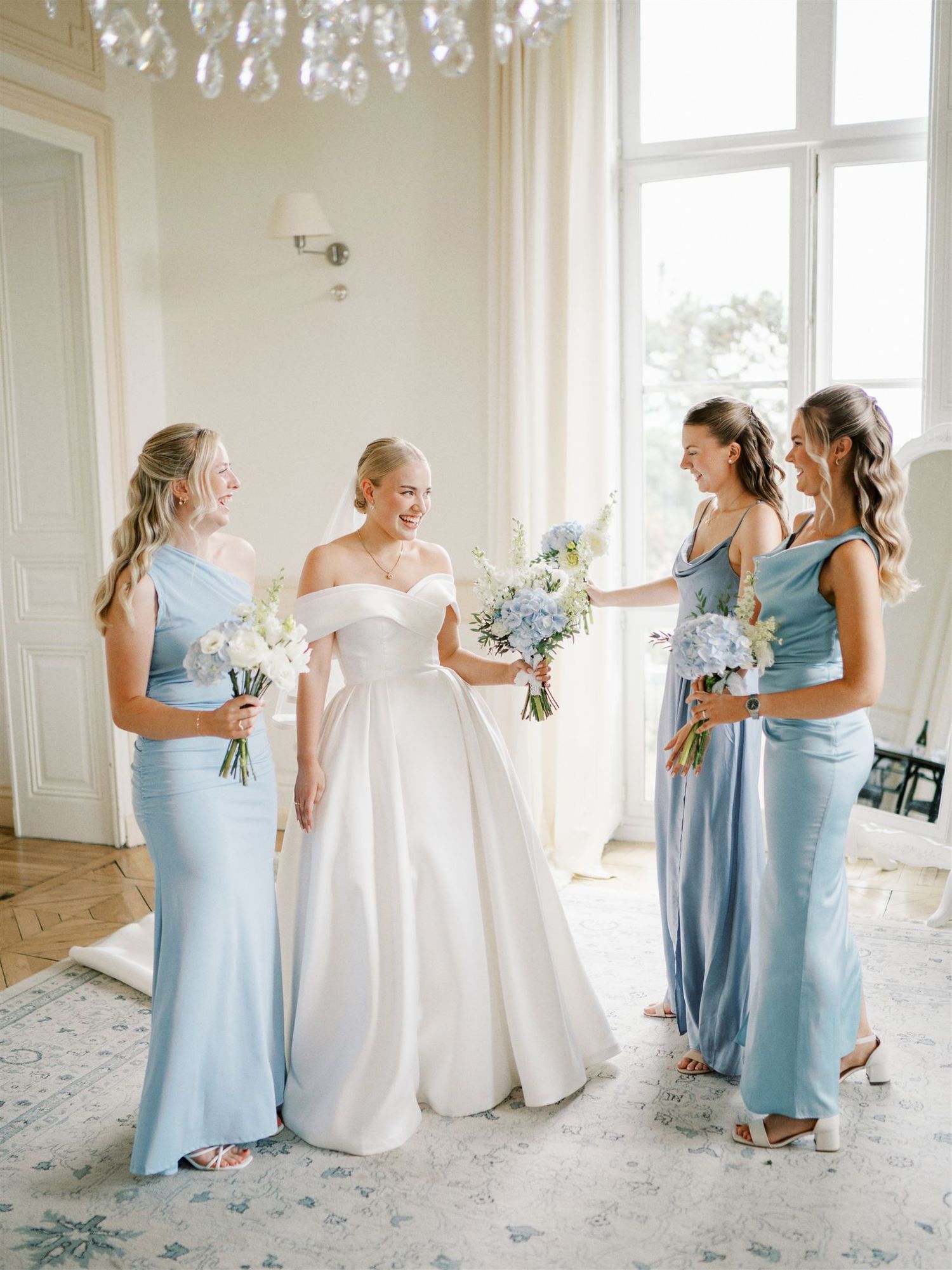 Bride in off-shoulder white ballgown with three bridesmaids in dusty blue satin dresses.