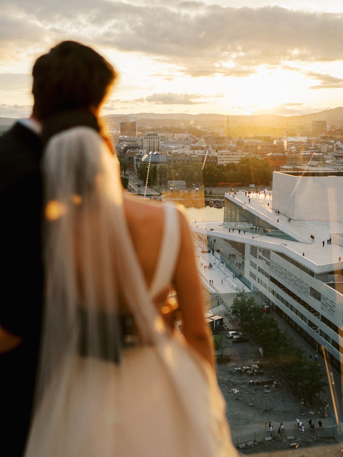 Bride and groom gazing at a golden sunset over a city skyline from a rooftop venue.