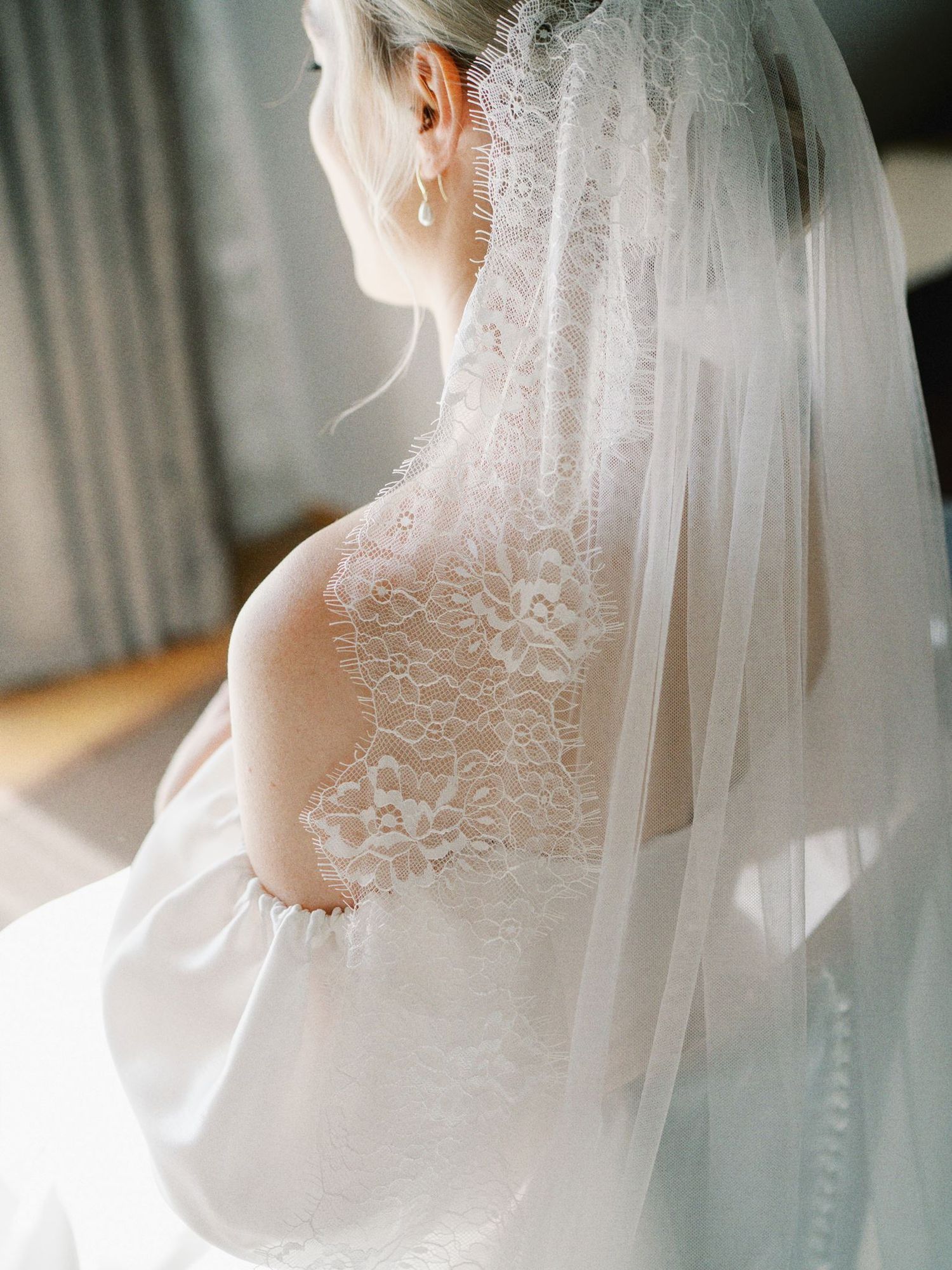 Bride in elegant lace wedding gown and veil, showcasing intricate floral lace back detail in soft natural light.