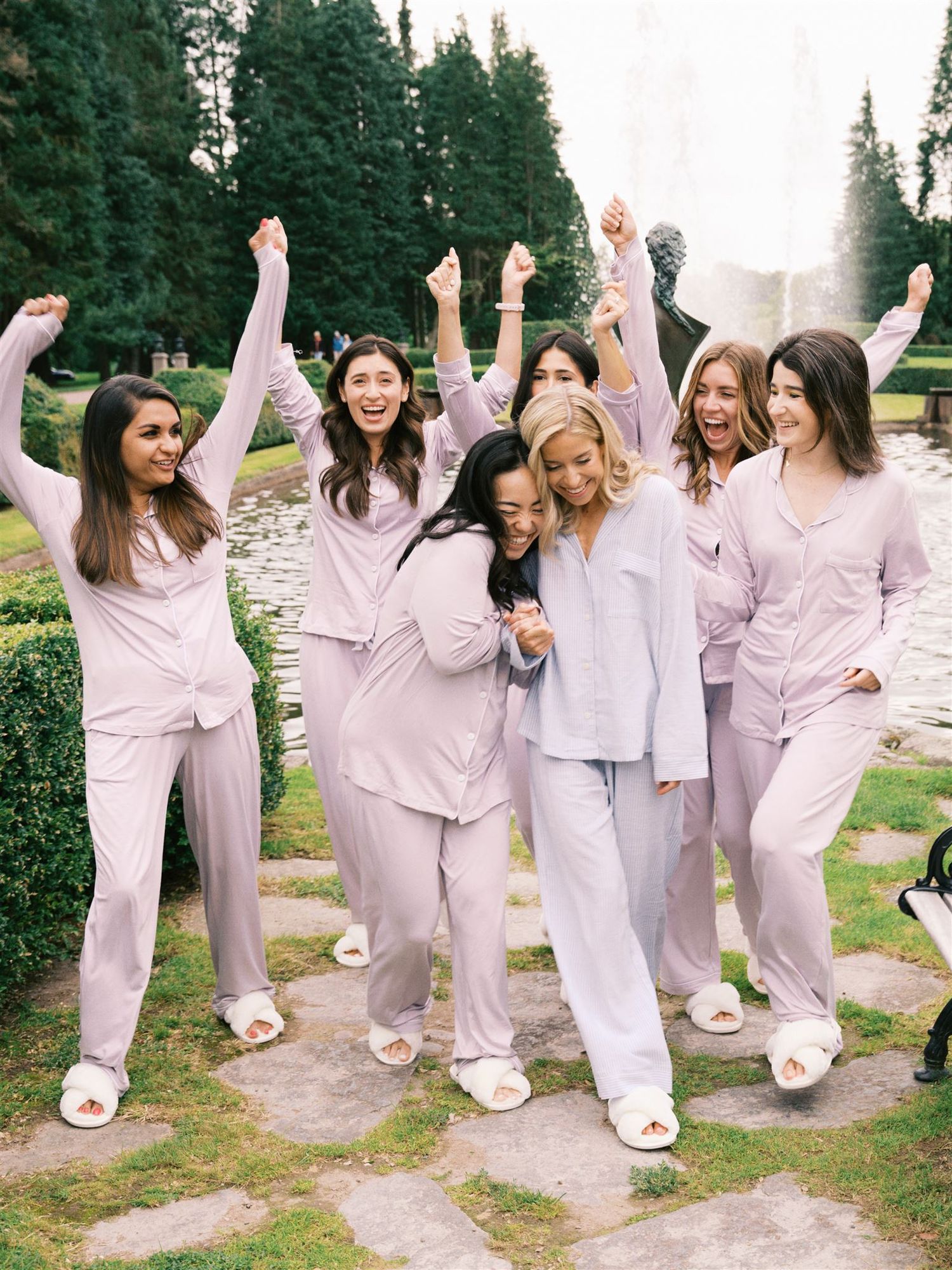 Bridesmaids in matching lavender pajamas celebrating joyfully in a formal garden setting.