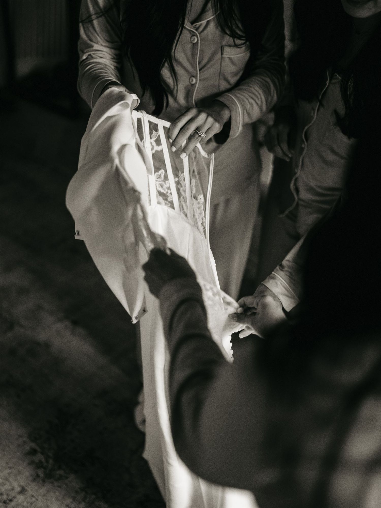 Black and white close-up of hands carefully handling a white lace wedding dress detail.