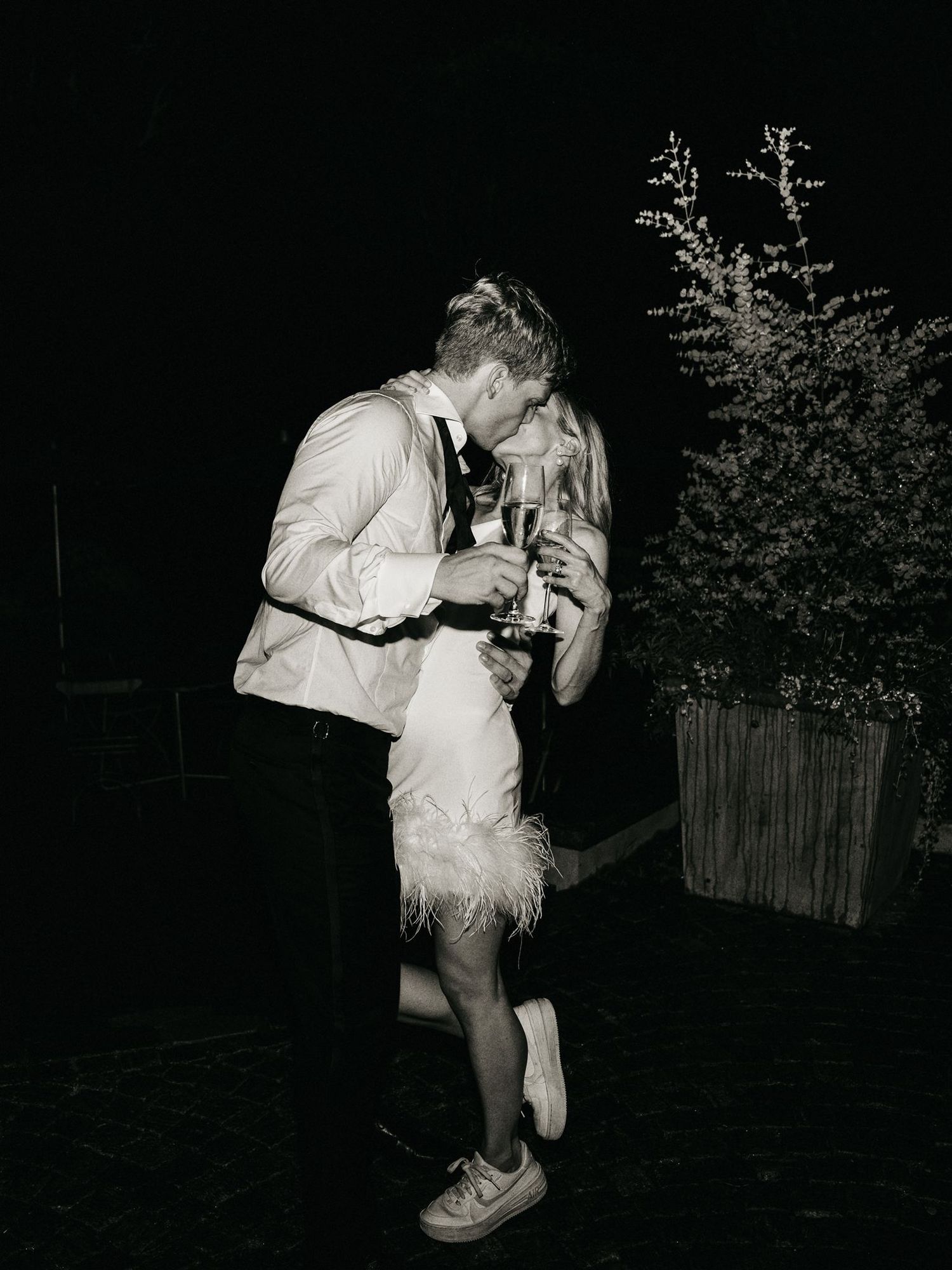 Black and white photo of newlyweds kissing outdoors at night after wedding reception.
