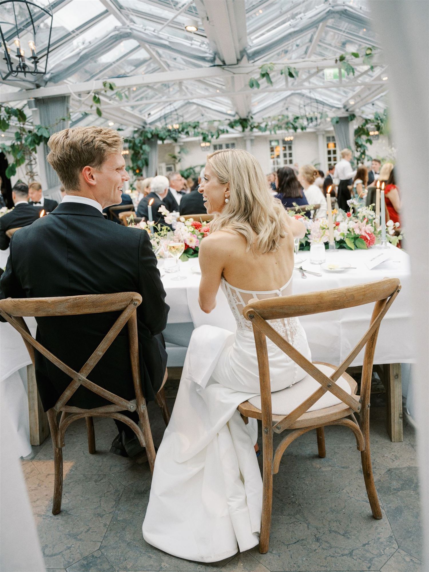 Bride and groom seated at sweetheart table in glass greenhouse wedding reception.