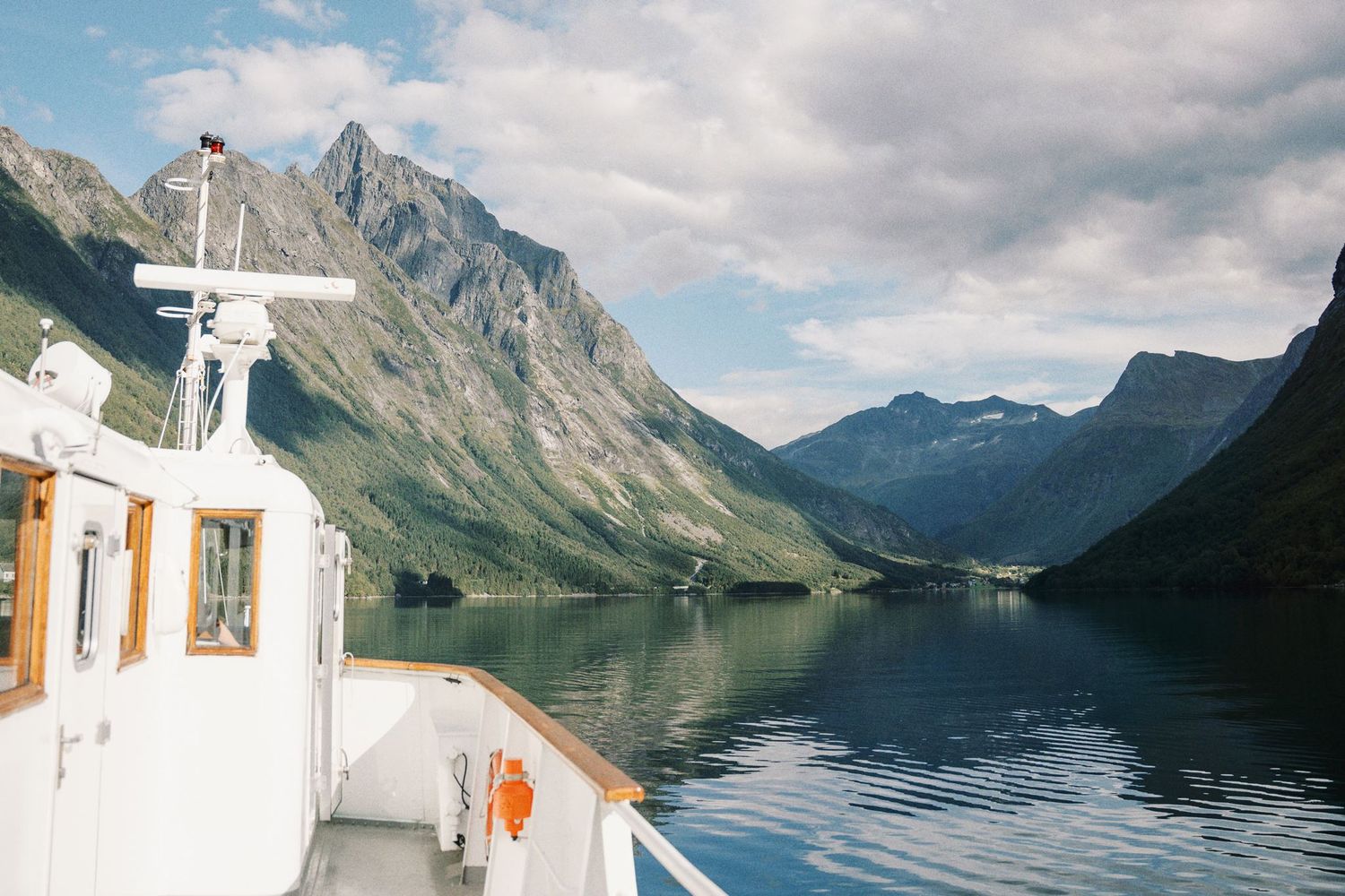 A scenic fjord cruise in Norway with mountains reflecting in calm blue waters under a partly cloudy sky.