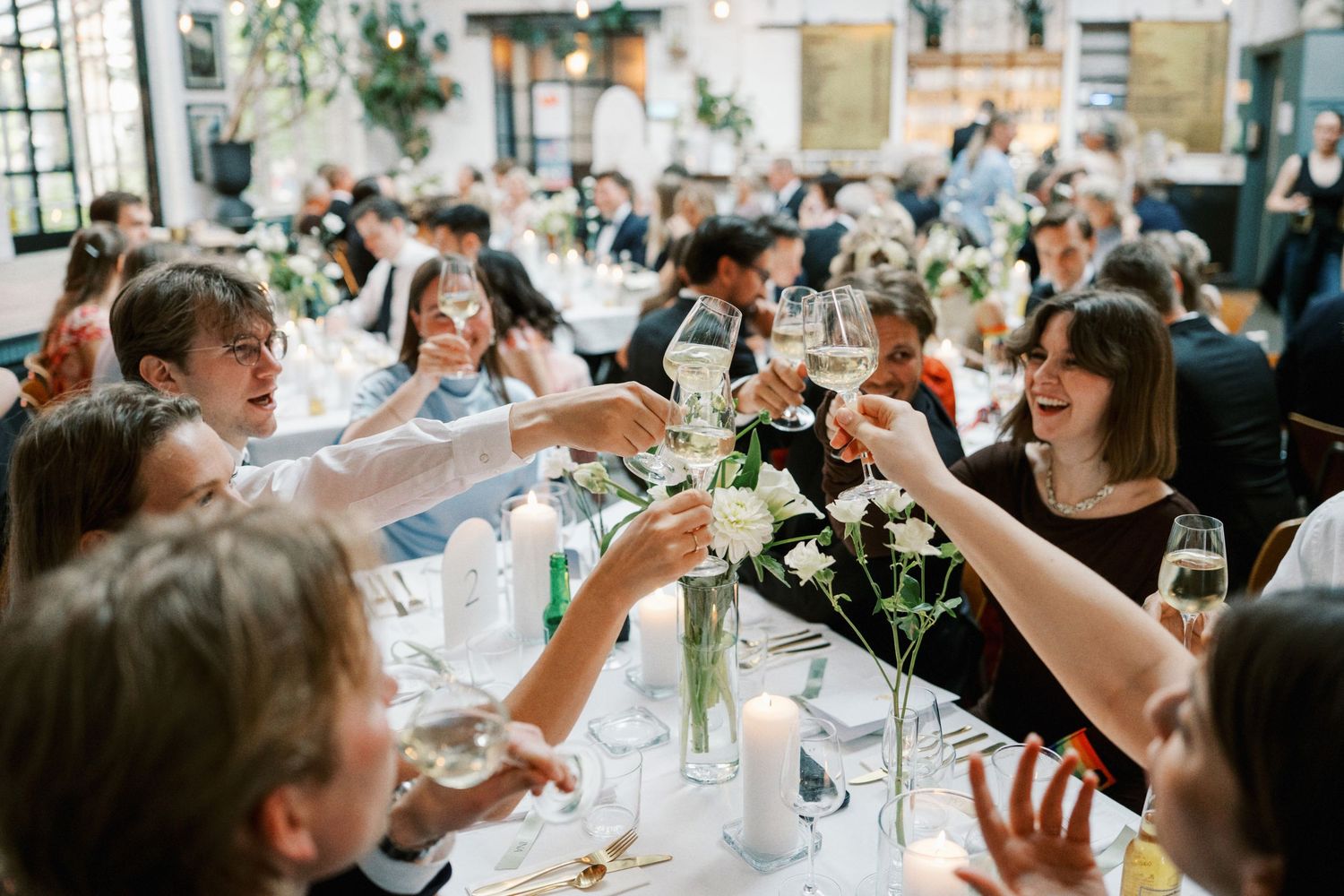 Wedding guests raising champagne glasses in a toast at an elegant reception with floral centerpieces.