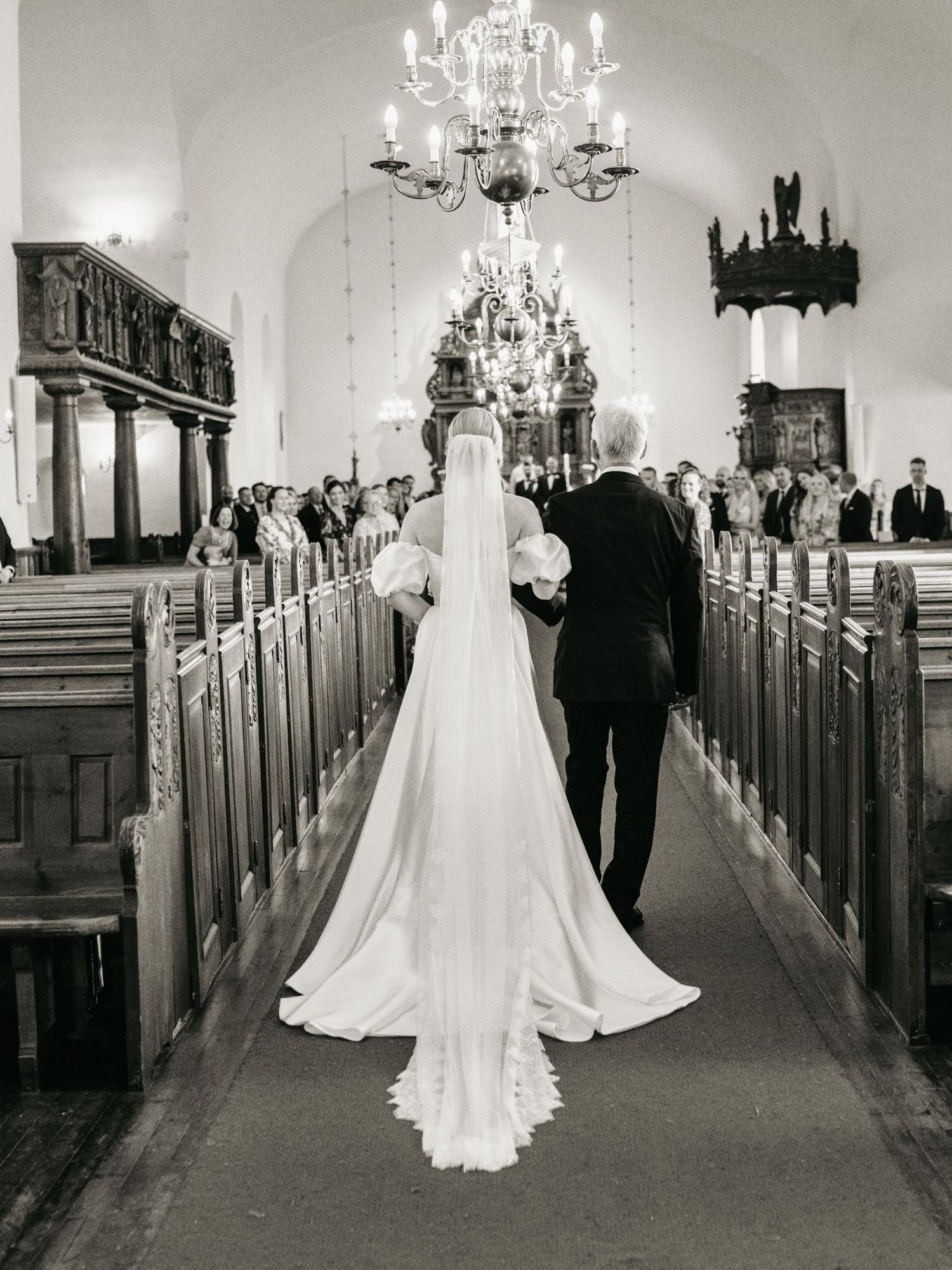 Black and white photo of a bride walking down the church aisle with her father on her wedding day.