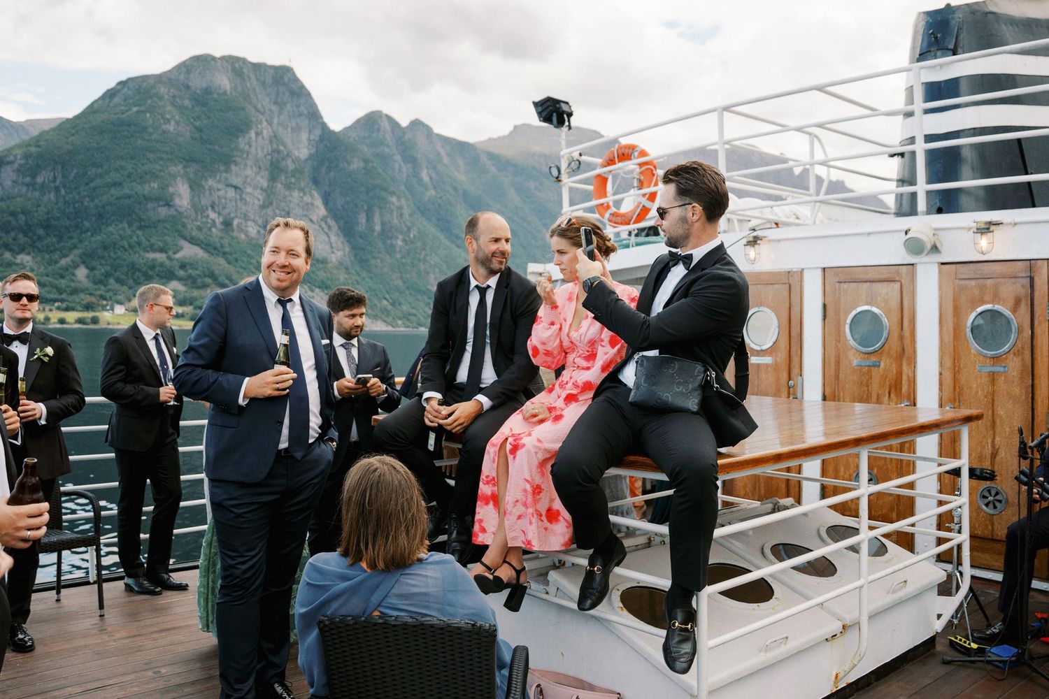 Wedding guests celebrate on a boat deck with stunning fjord and mountain views in Norway.