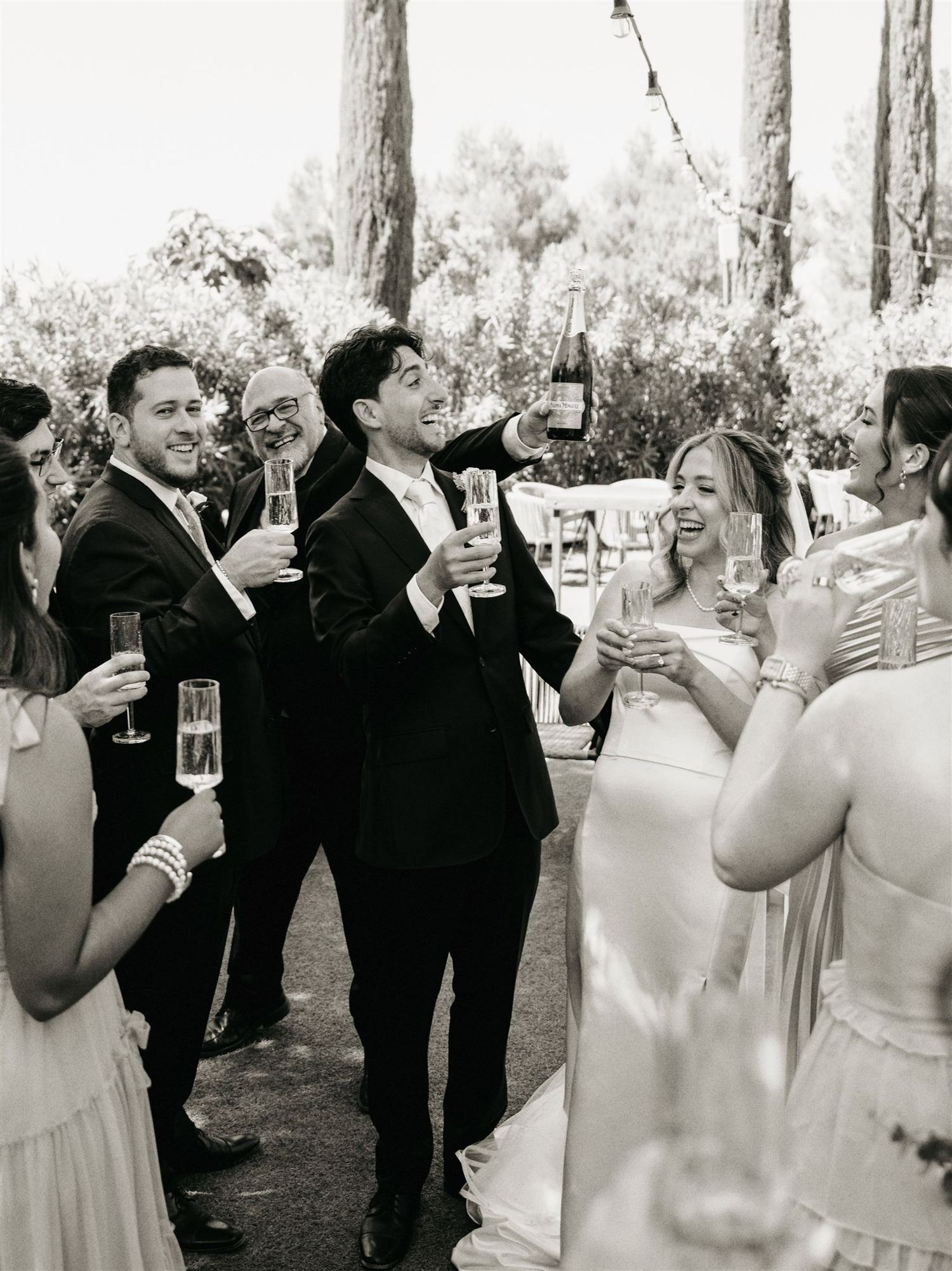 Wedding party toasting with champagne glasses outdoors in black and white celebration photo.