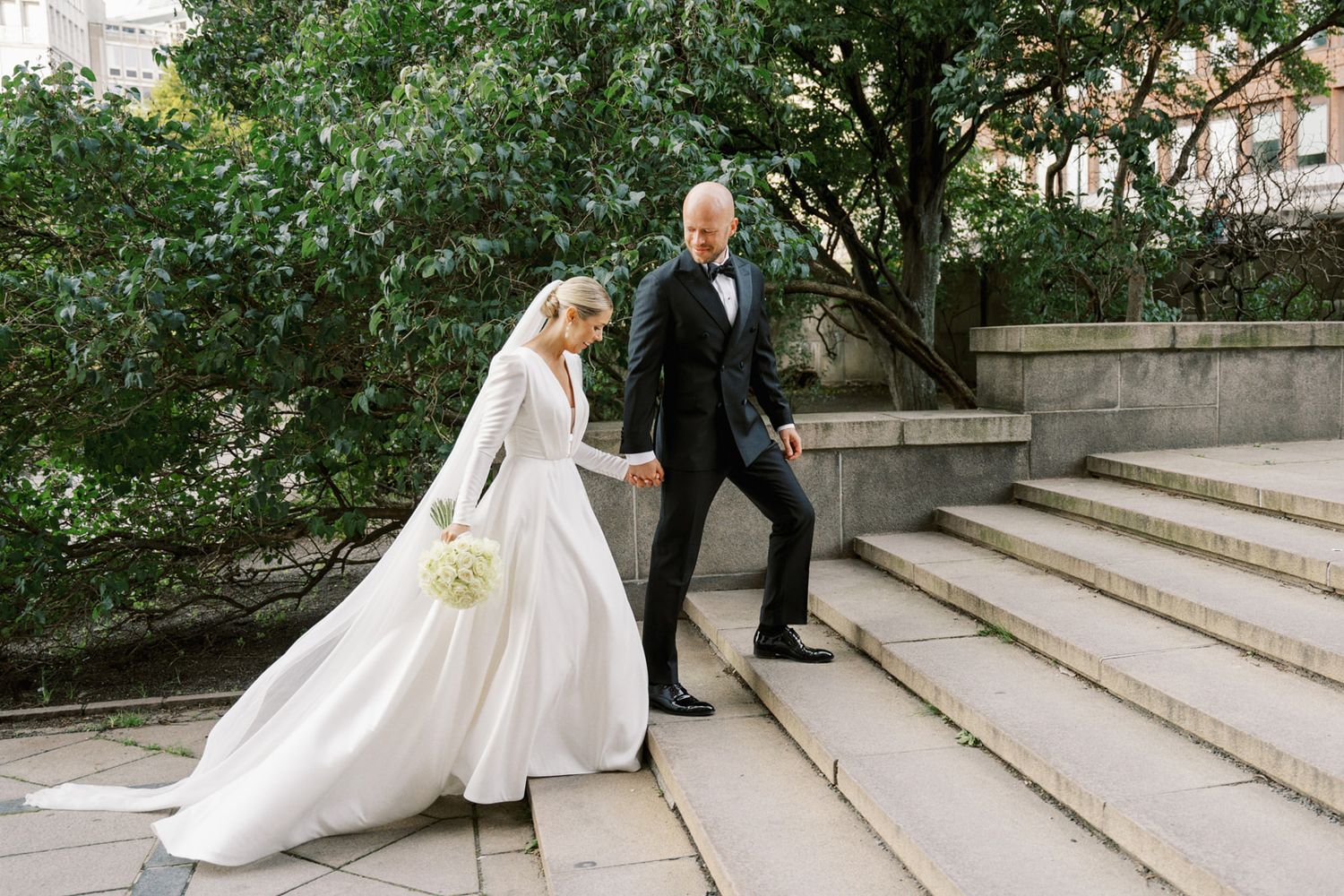 Bride and groom walking up stone steps surrounded by lush greenery on wedding day.
