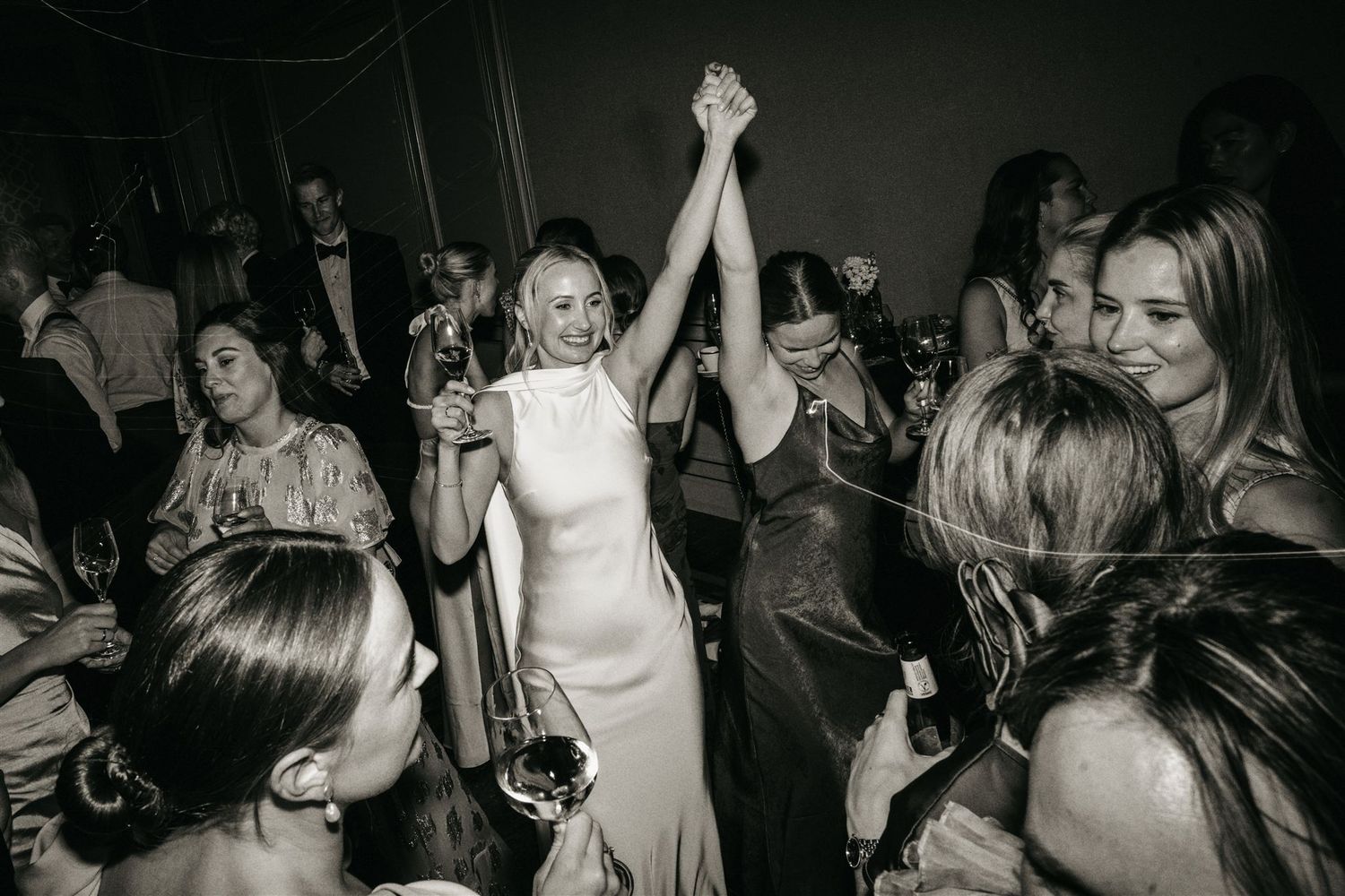Bride dancing joyfully with guests at wedding reception in black and white photo.