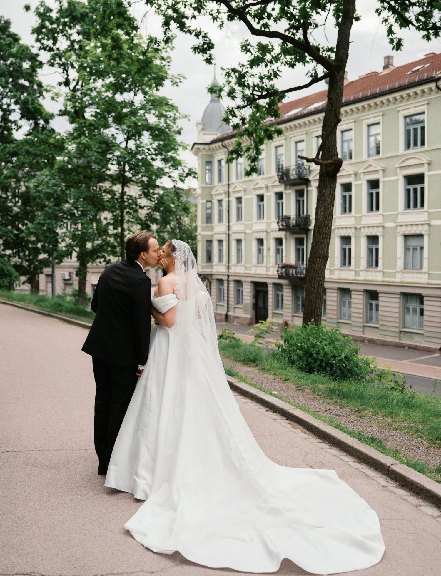 Bride and groom kissing in front of a classic European building, bride wearing a long white gown with veil.
