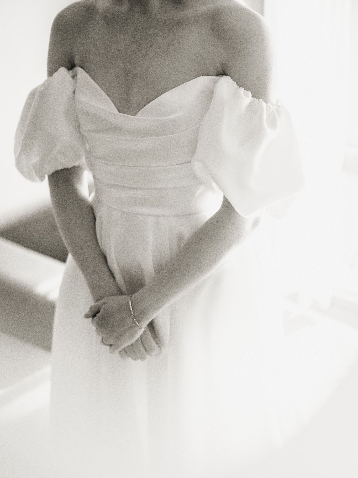 Bride wearing an elegant off-shoulder white wedding gown with puff sleeves and draped bodice.