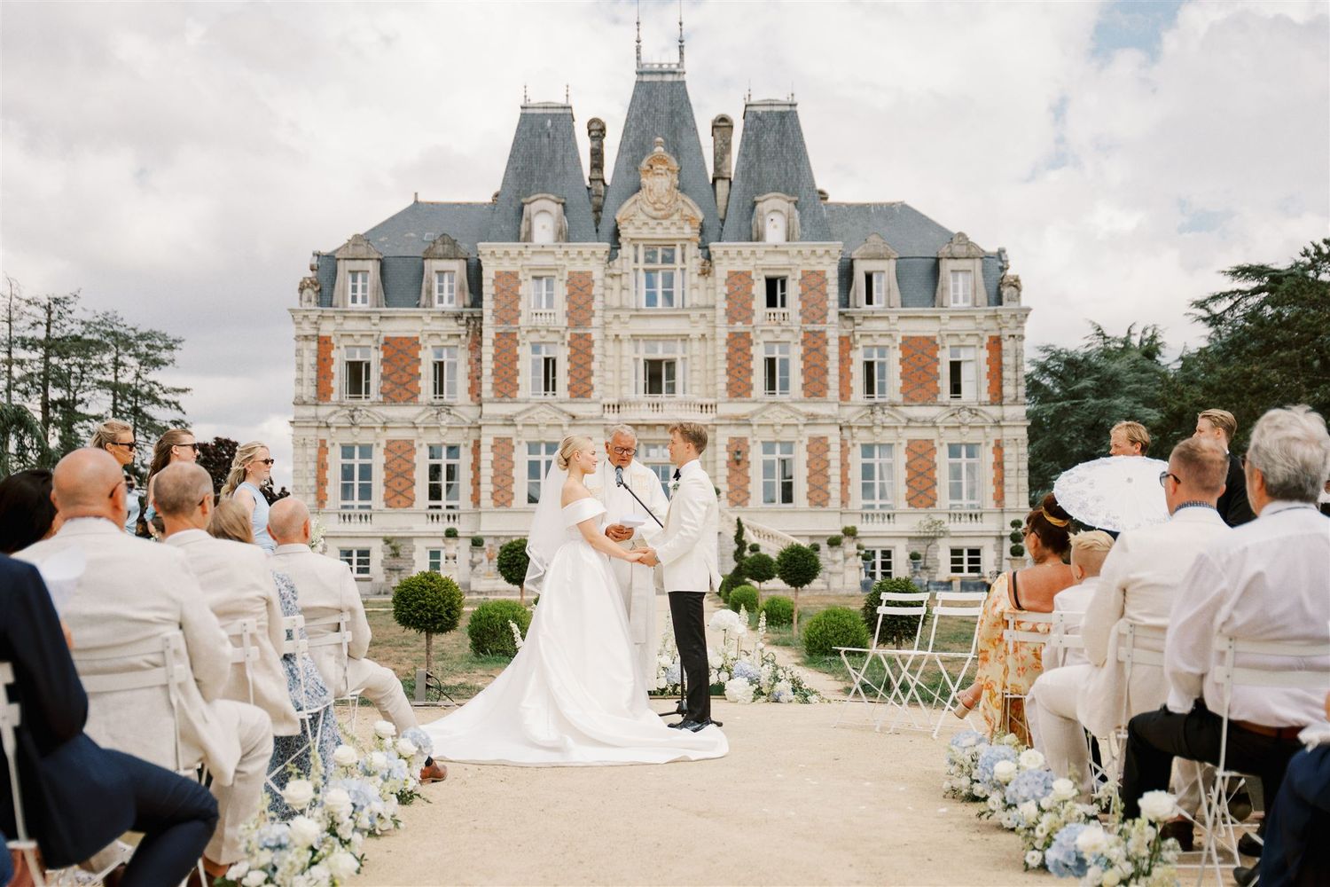 Outdoor wedding ceremony in front of stunning French chateau with guests seated on both sides.
