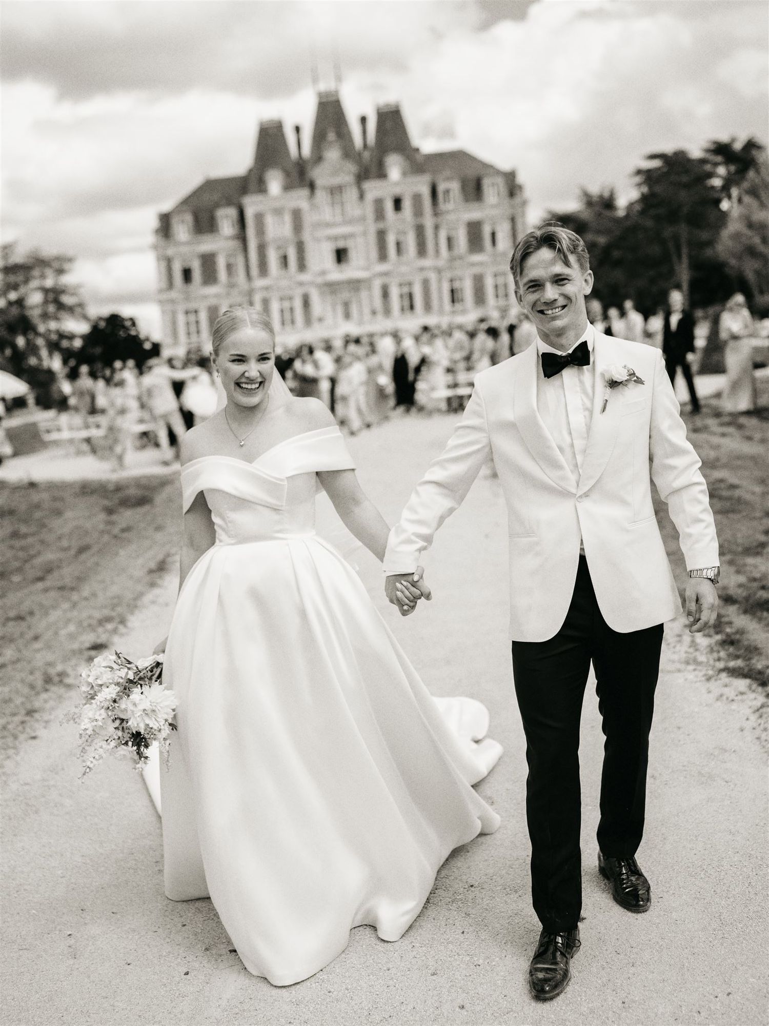 Newlyweds holding hands walking from chateau in black and white wedding portrait photo.