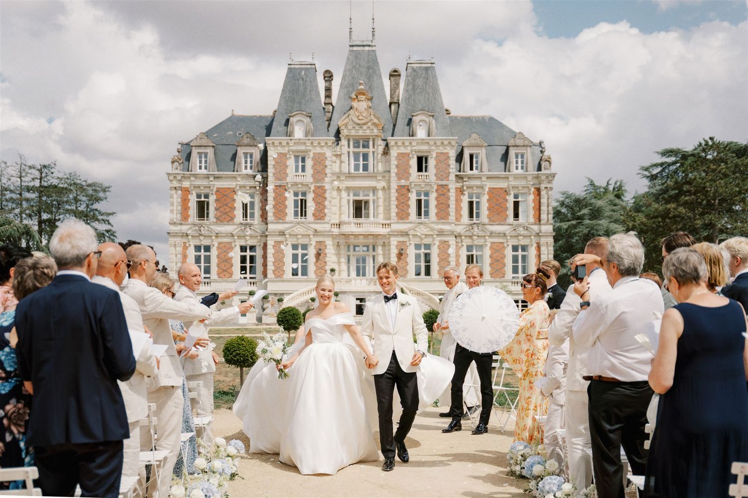 Joyful bride and groom recessional in front of grand French chateau surrounded by cheering guests.
