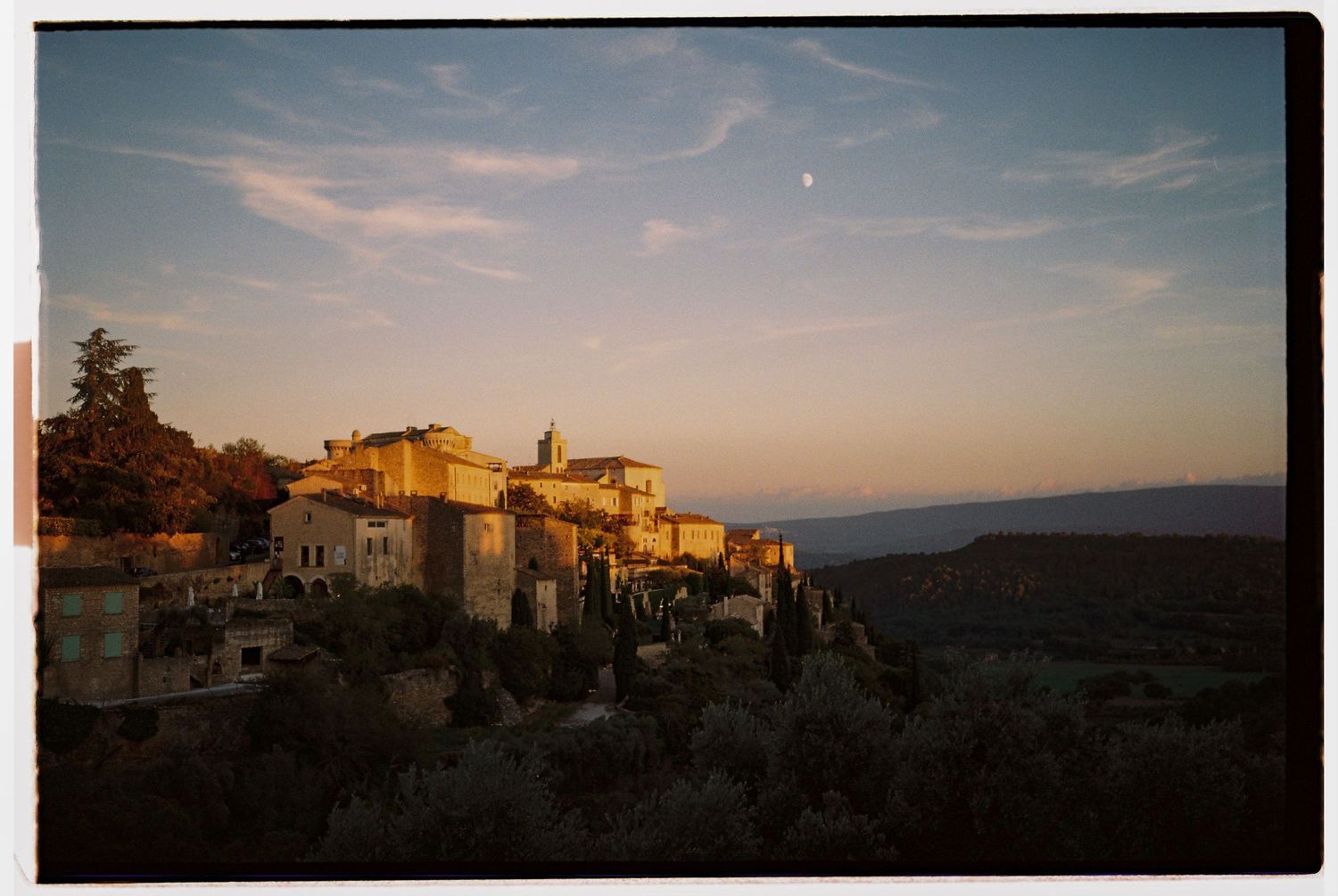 Golden sunset over Gordes in Provence illuminates ancient hilltop village with stone buildings overlooking vast valley under twilight sky.