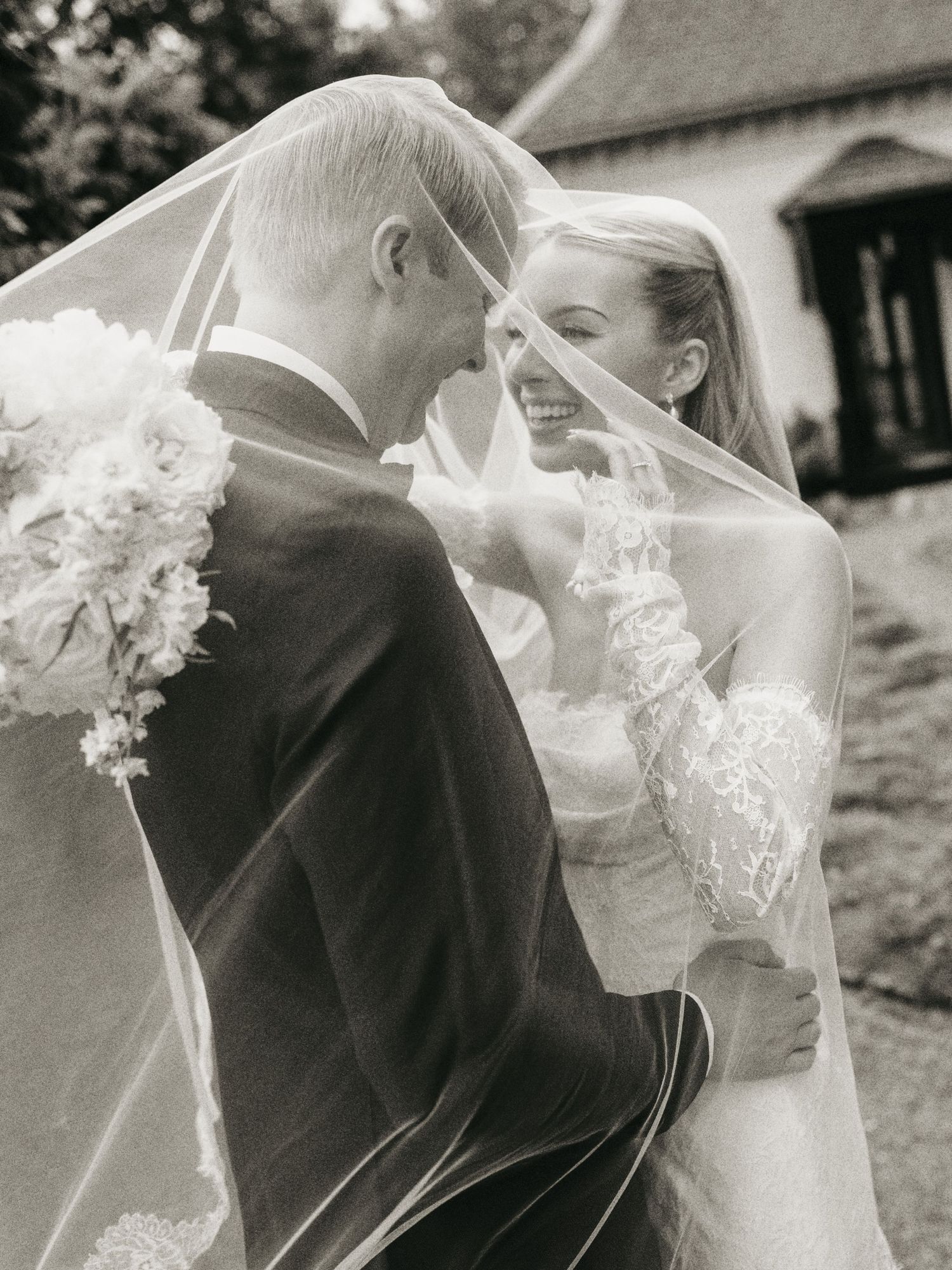 Black and white wedding photo of bride and groom sharing a romantic moment under a flowing veil.