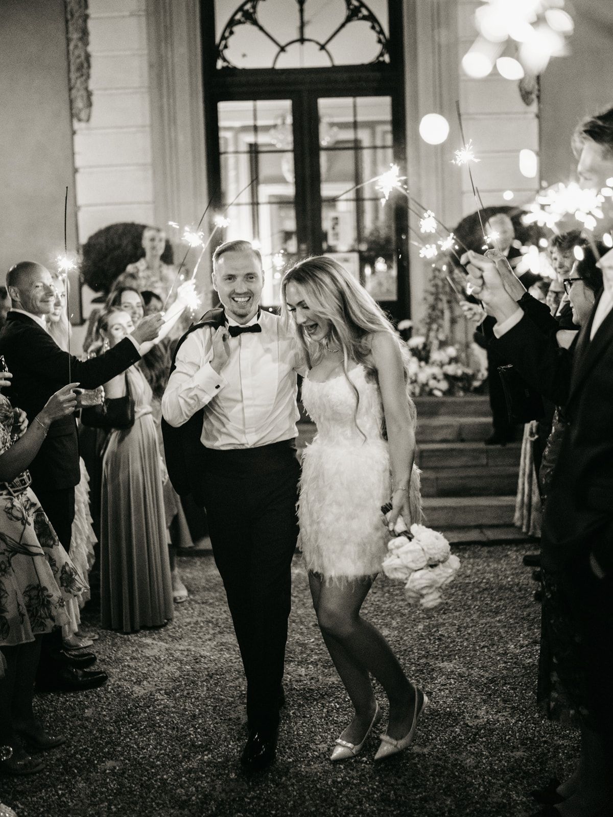 Couple exits wedding reception through sparkler tunnel in black and white photo.