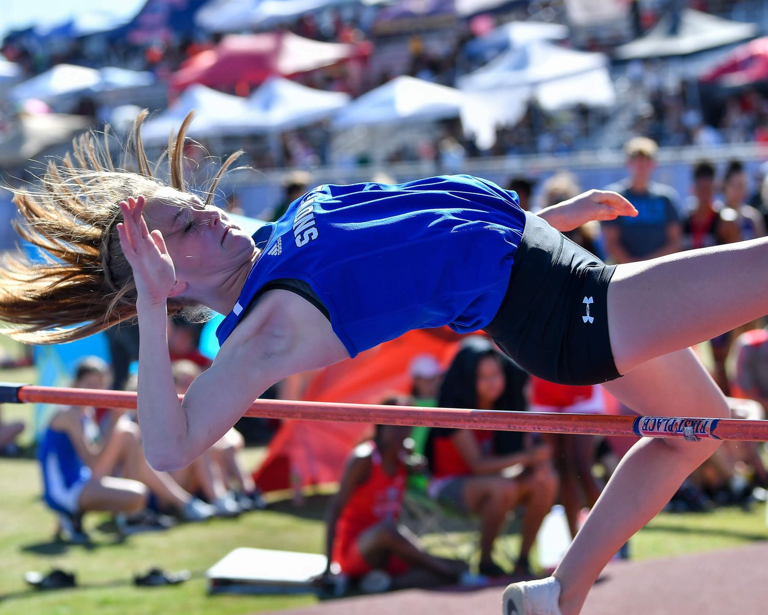 Athlete performs high jump using Fosbury Flop technique at outdoor track meet.